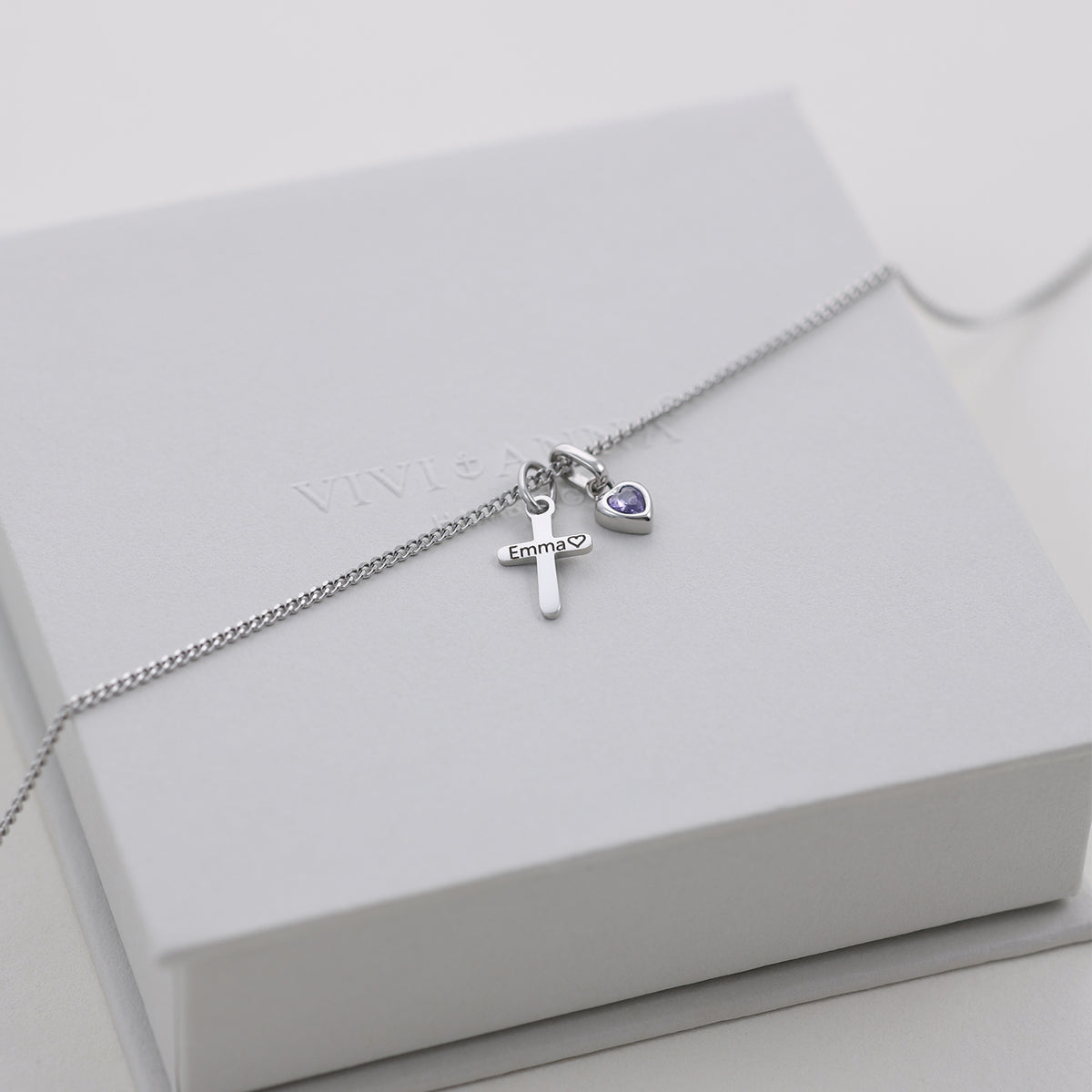 Silberne Kreuzkette mit Gravur 'Emma' und violettem Geburtsstein auf weißer Schmuckbox