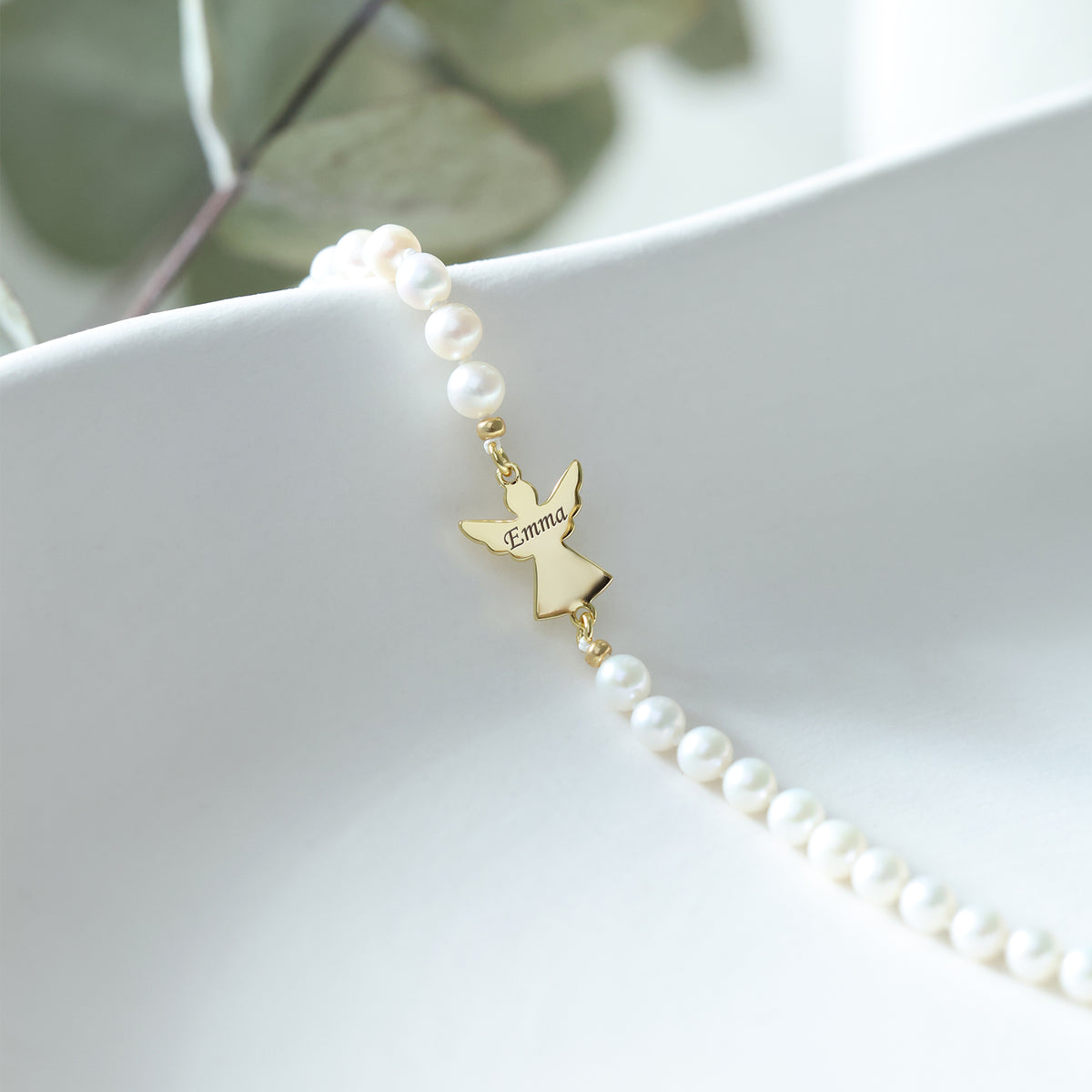 Perlenarmband mit graviertem Goldengel 'Emma' auf weißer Schale mit Eukalyptus