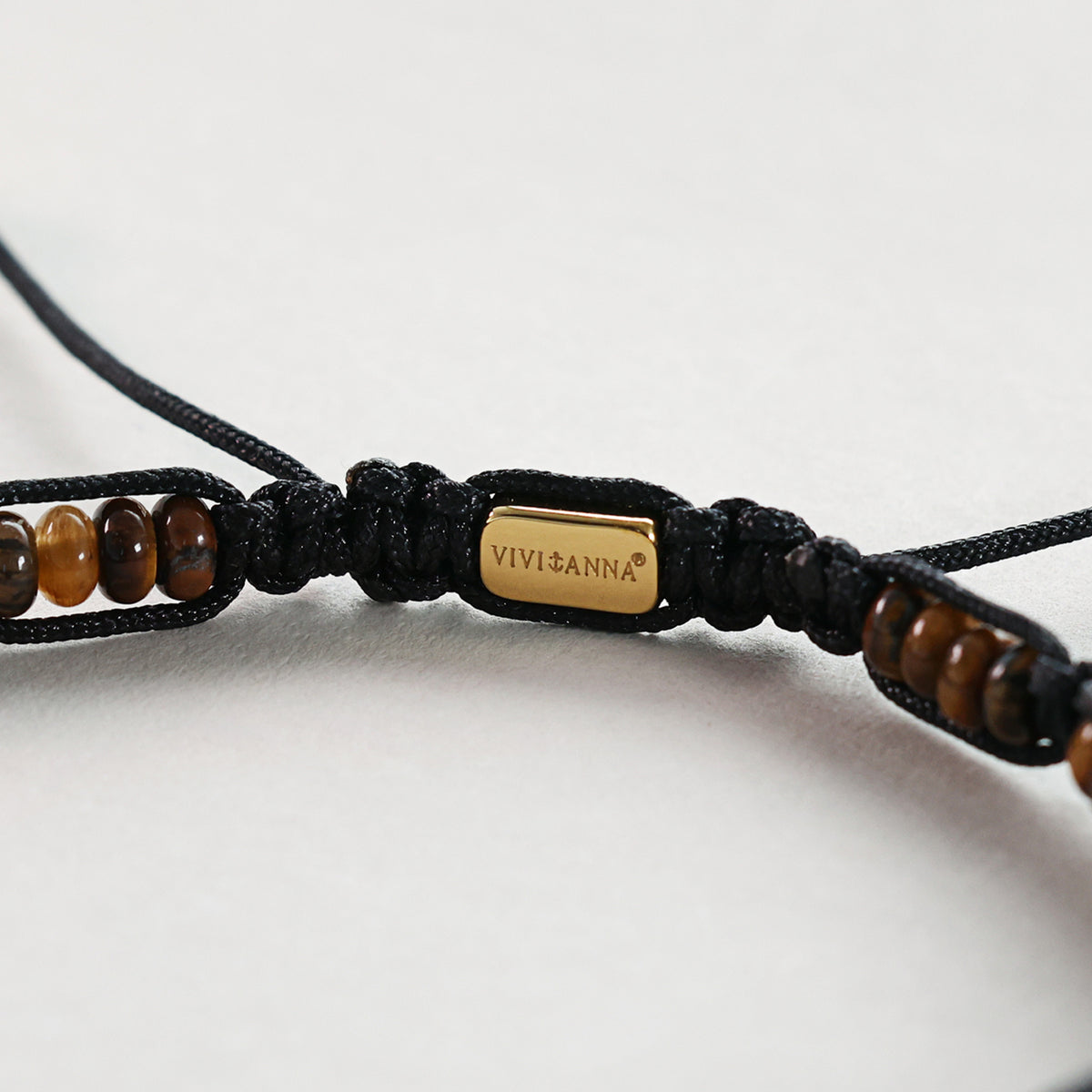 Nahaufnahme der Markenplakette VIVI&ANNA zwischen Tigerauge-Perlen am Armband