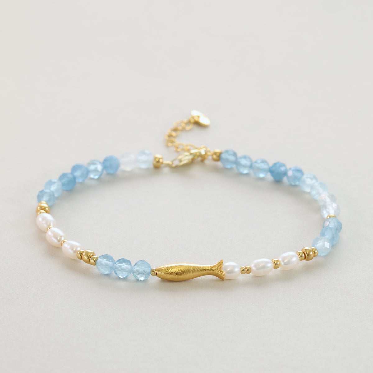 Fisch-Armband mit Aquamarin und Süßwasserperlen in Gold, Nahaufnahme auf hellem Untergrund