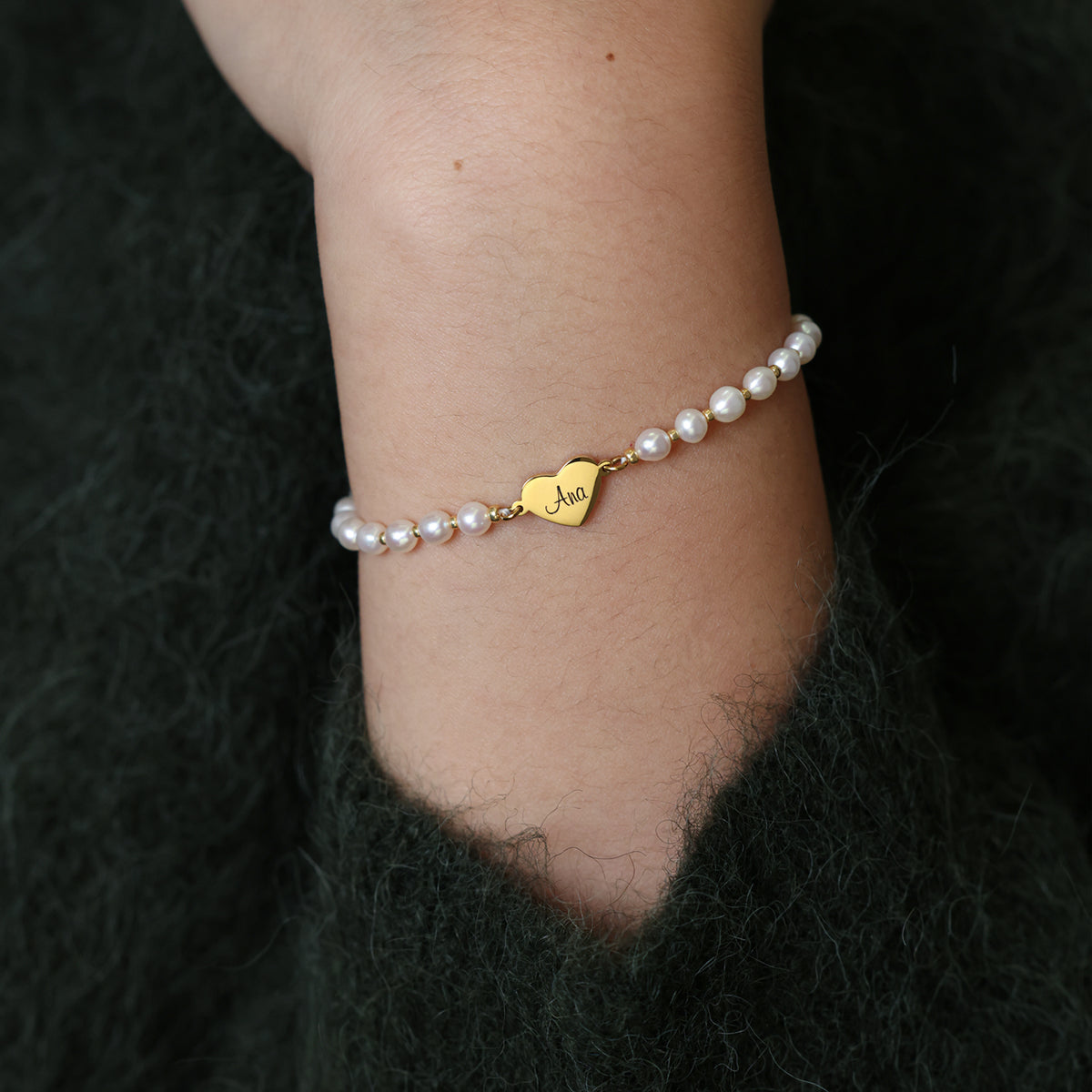 Person trägt Süßwasser-Perlenarmband mit goldenem Herz-Anhänger am Handgelenk