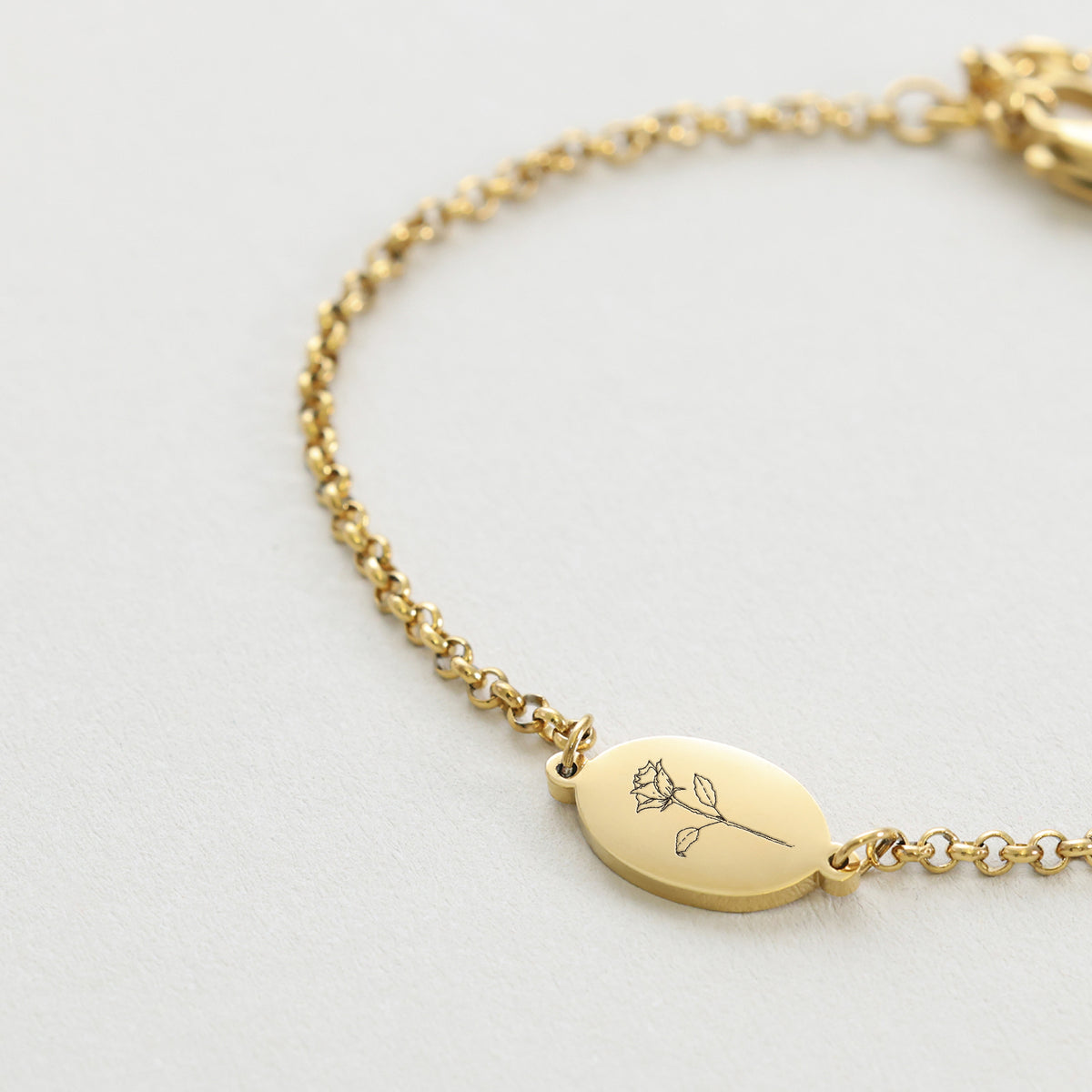 Nahaufnahme des ovalen Gravurplättchens mit Blumenmotiv am Geburtsblumen-Armband in Gold