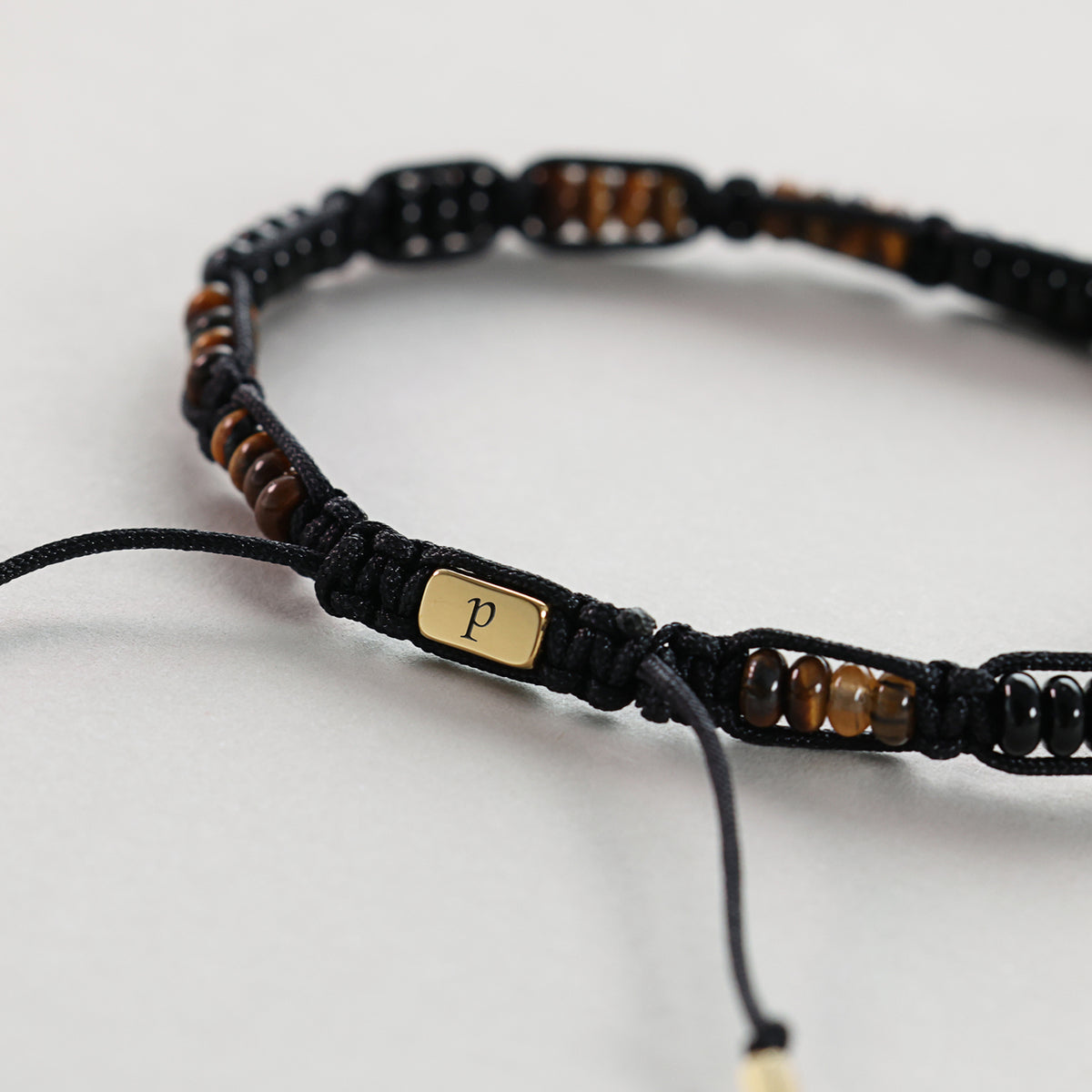Nahaufnahme der goldenen Gravurplakette mit Initiale P am Tigerauge Armband