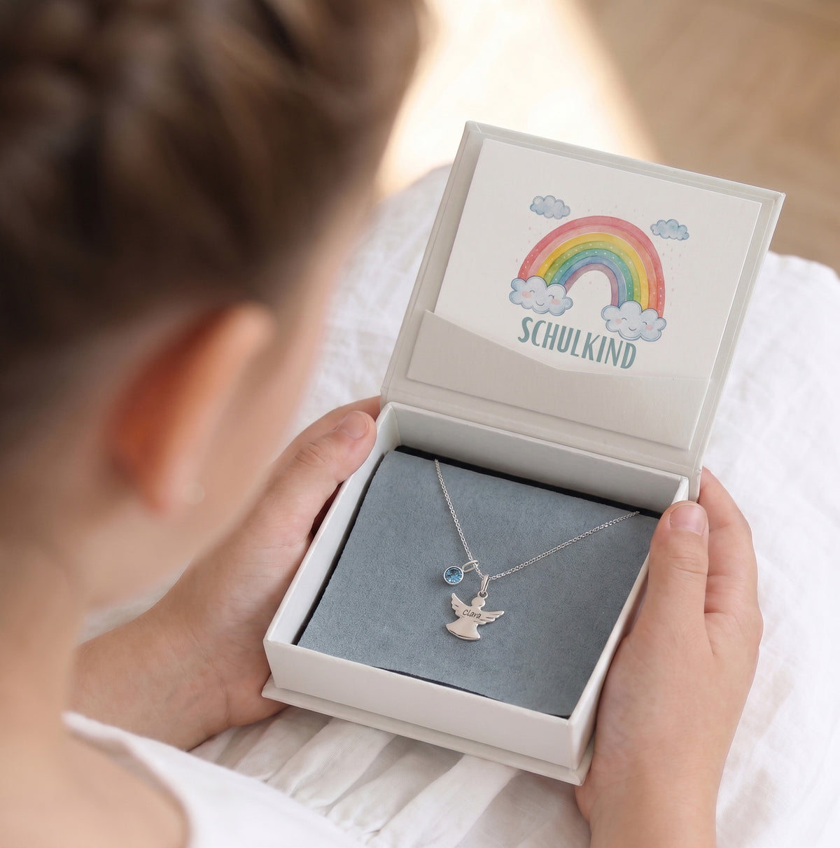Mädchen öffnet Geschenkbox mit Schutzengel Halskette in Silber und Geburtsstein-Anhänger