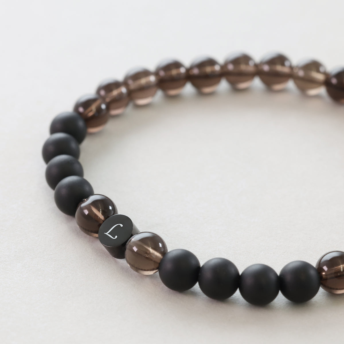 Nahaufnahme: graviertes Buchstaben-Element L am Naturstein-Armband aus Rauchquarz und Onyx