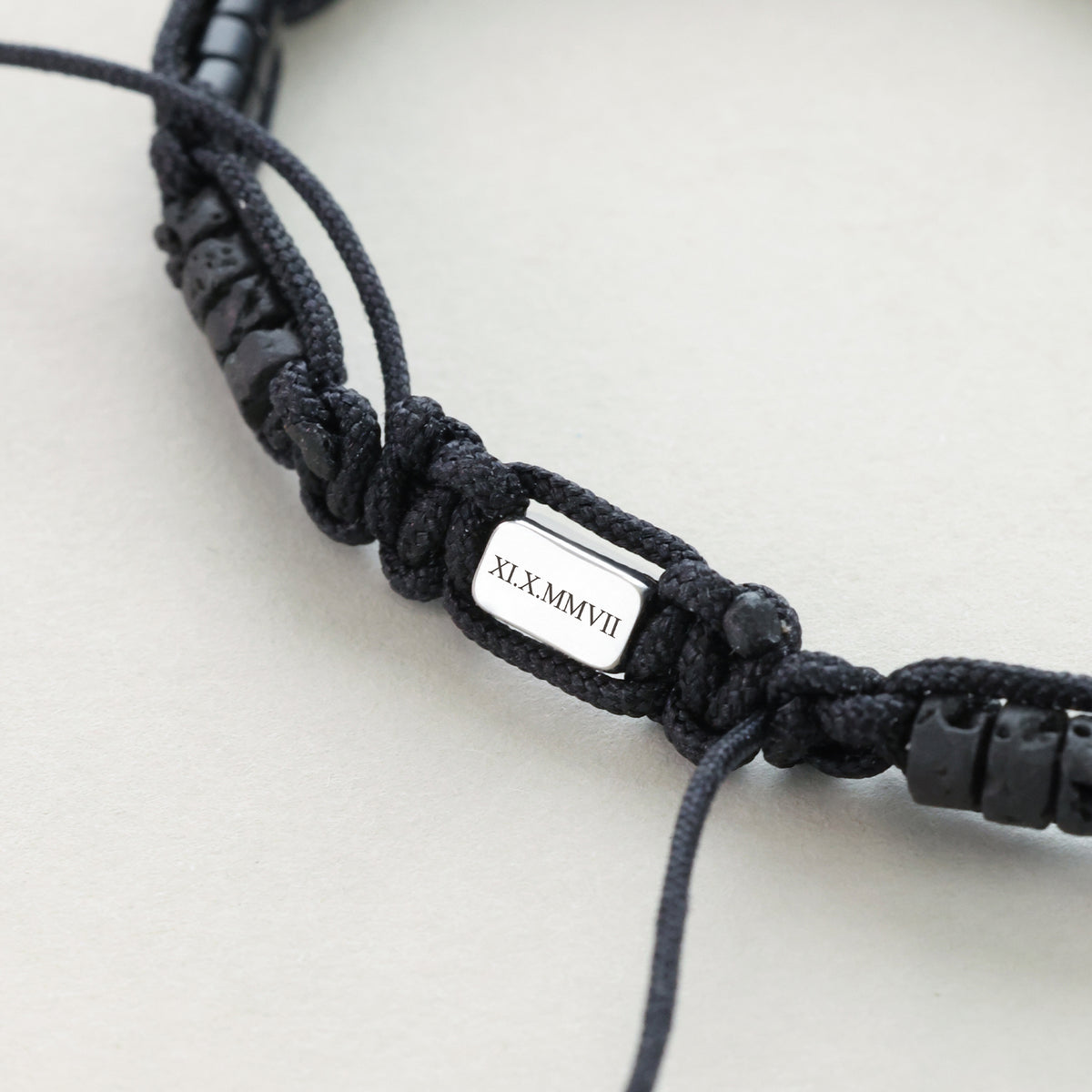 Nahaufnahme der gravierten Plakette mit römischem Datum XI.X.MMVII am Makramee Armband