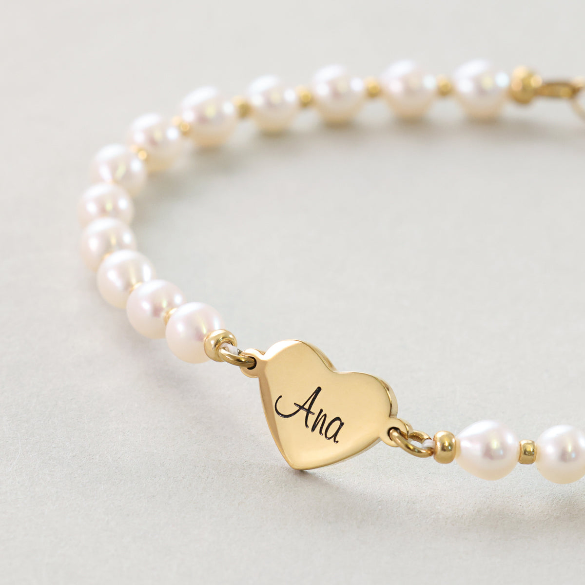 Nahaufnahme des goldenen Herz-Anhängers mit Gravur Ana am Perlenarmband