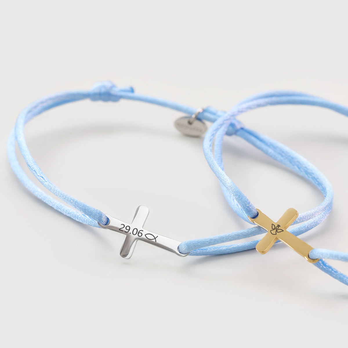 Zwei Satinarmbänder mit Kreuz-Anhänger in Silber und Gold, graviert mit Datum und Symbol