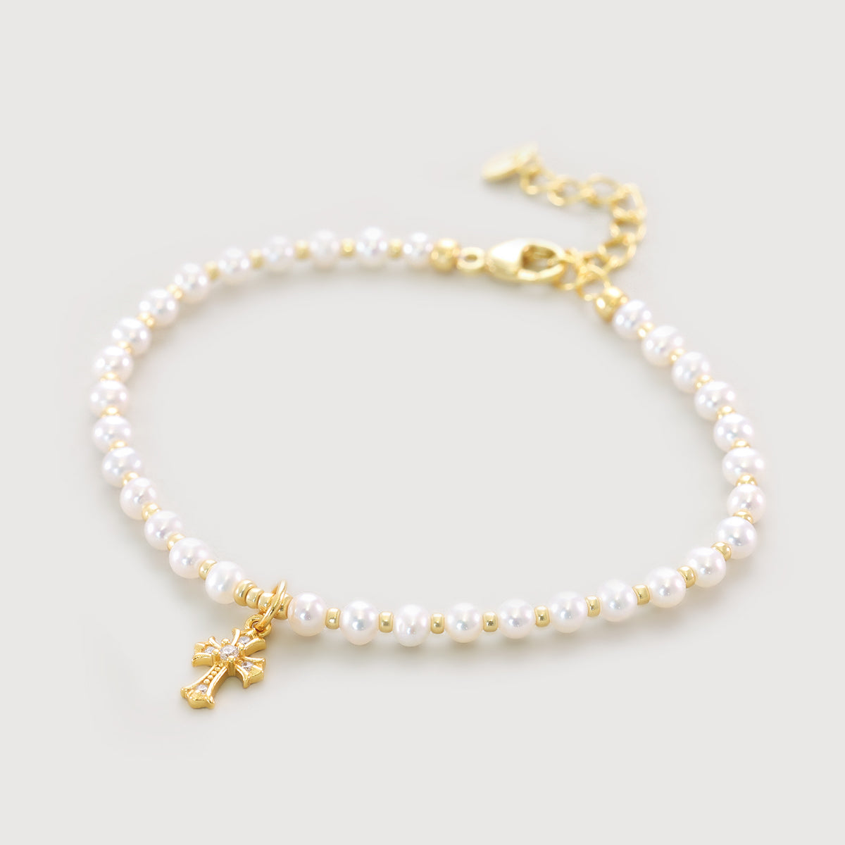 Süßwasserperlen Armband mit funkelndem Kreuz in Gold, freigestellt auf weißem Hintergrund