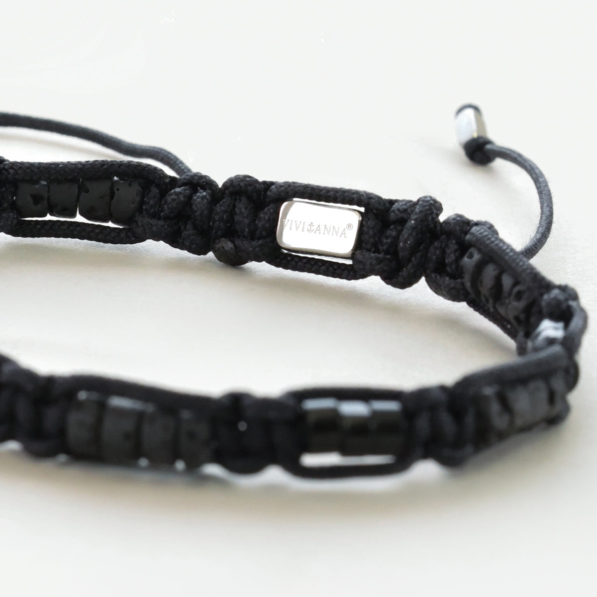Nahaufnahme der Markenplakette VIVI&ANNA am schwarzen Makramee Armband mit Lava-Perlen