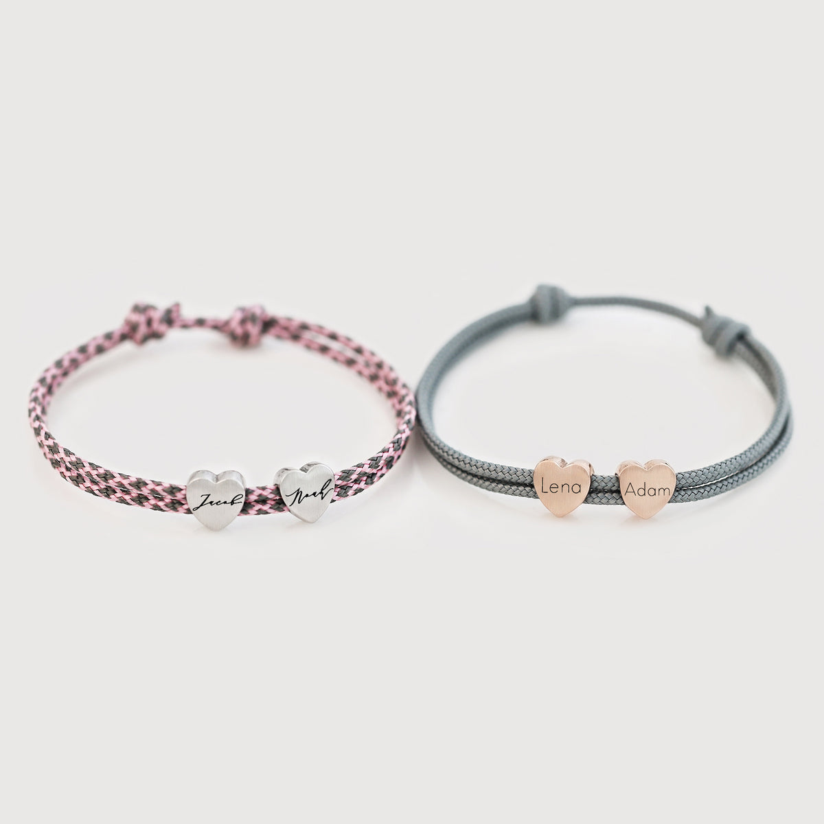 Zwei personalisierte Herzarmbänder aus Segeltau – rosa-schwarz mit Namen 'Zeek' und 'Noah', grau mit Namen 'Lena' und 'Adam'