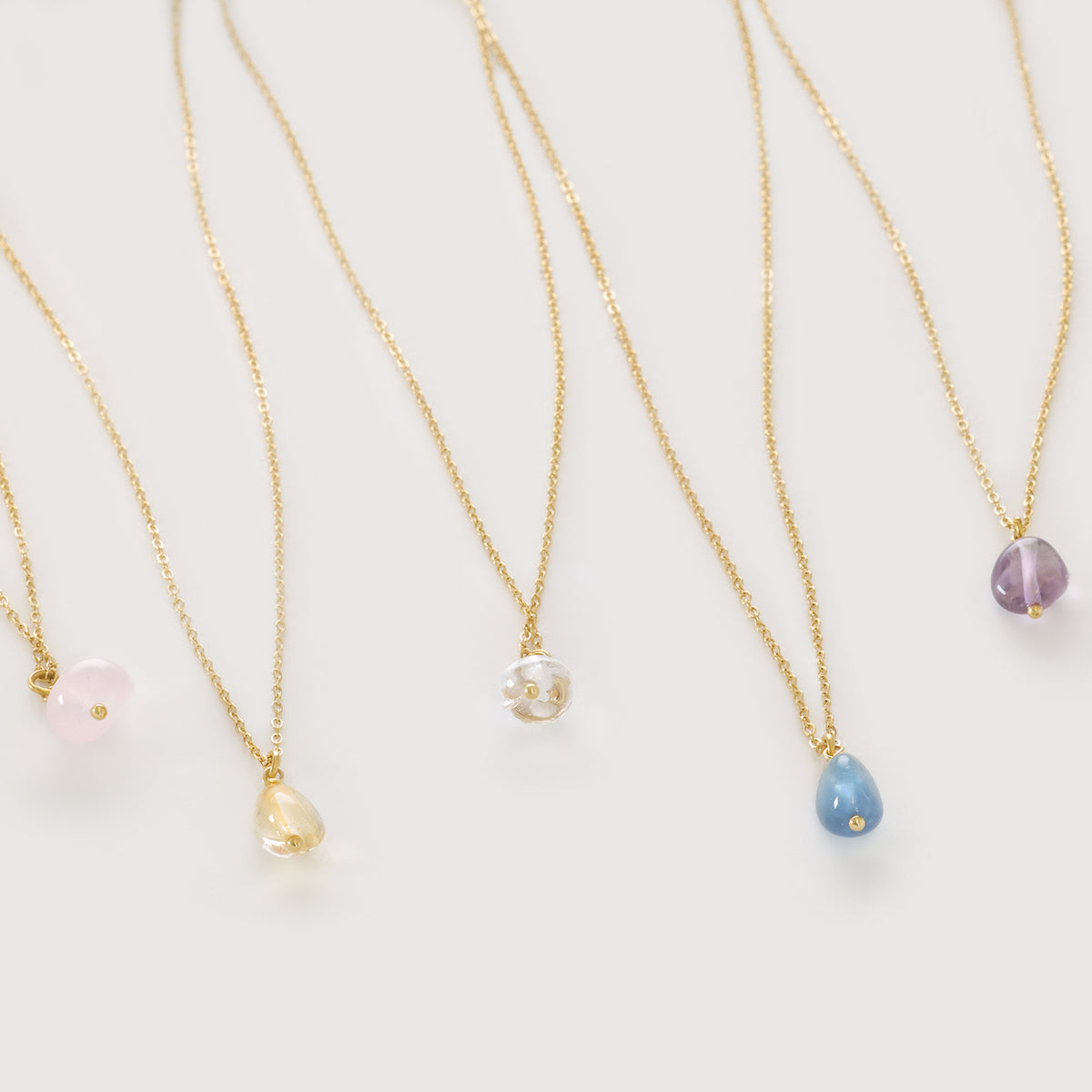 Minimalistische Glücksstein-Halskette in fünf Farben nebeneinander – Rosa, Gelb, Klar, Blau und Lila
