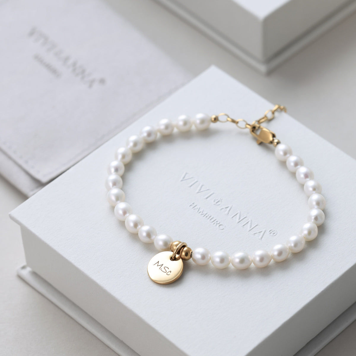 Perlenarmband mit Gravurplättchen auf Schmuckbox, mit Stoffbeutel im Hintergrund