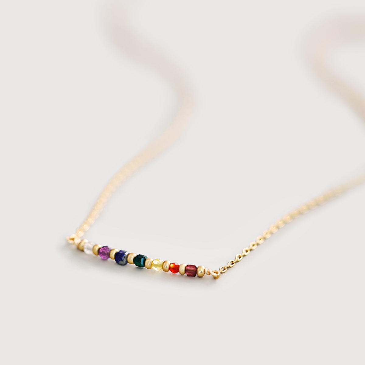 Chakra-Heilsteinkette in Gold mit bunten Edelstein-Perlen, Nahaufnahme auf hellem Untergrund