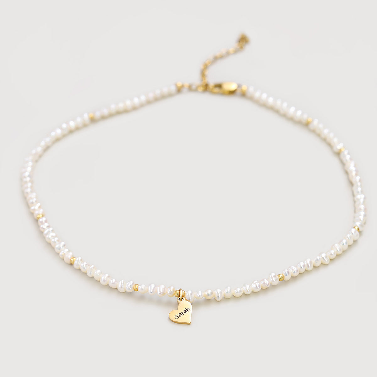 Perlenkette mit personalisierbarem Herzanhänger in Gold, flach liegend mit graviertem Namen Sarah