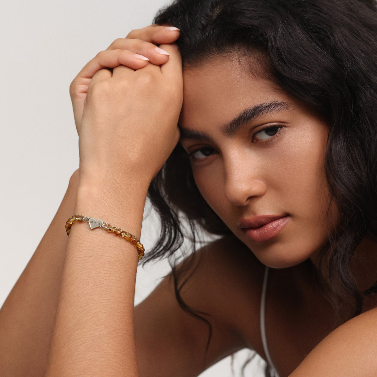 Frau trägt Bernstein-Perlenarmband mit kleinem goldenem Herzanhänger am Handgelenk