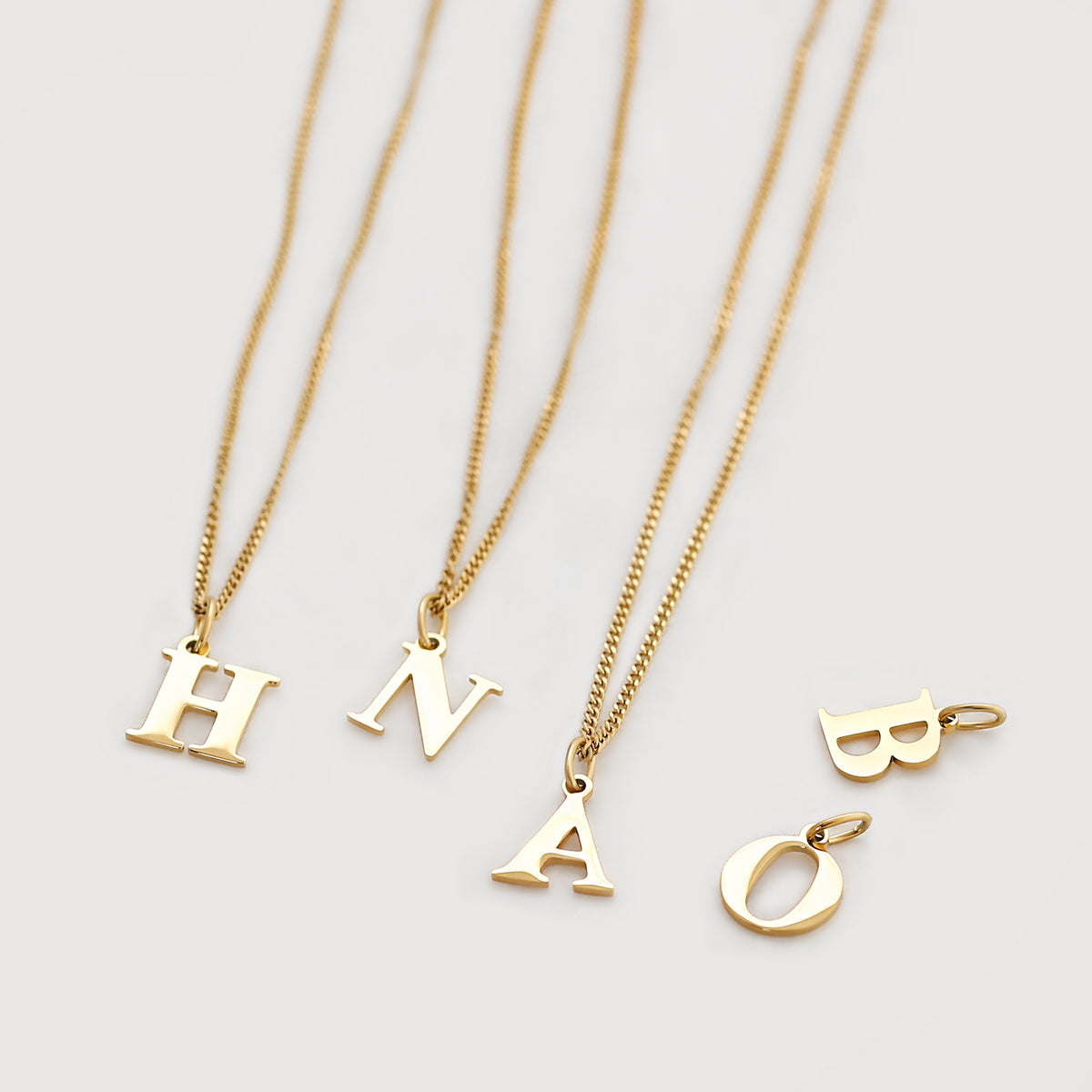 Vier goldene Buchstaben-Anhänger H, N, A und O/B mit dünnen Ketten