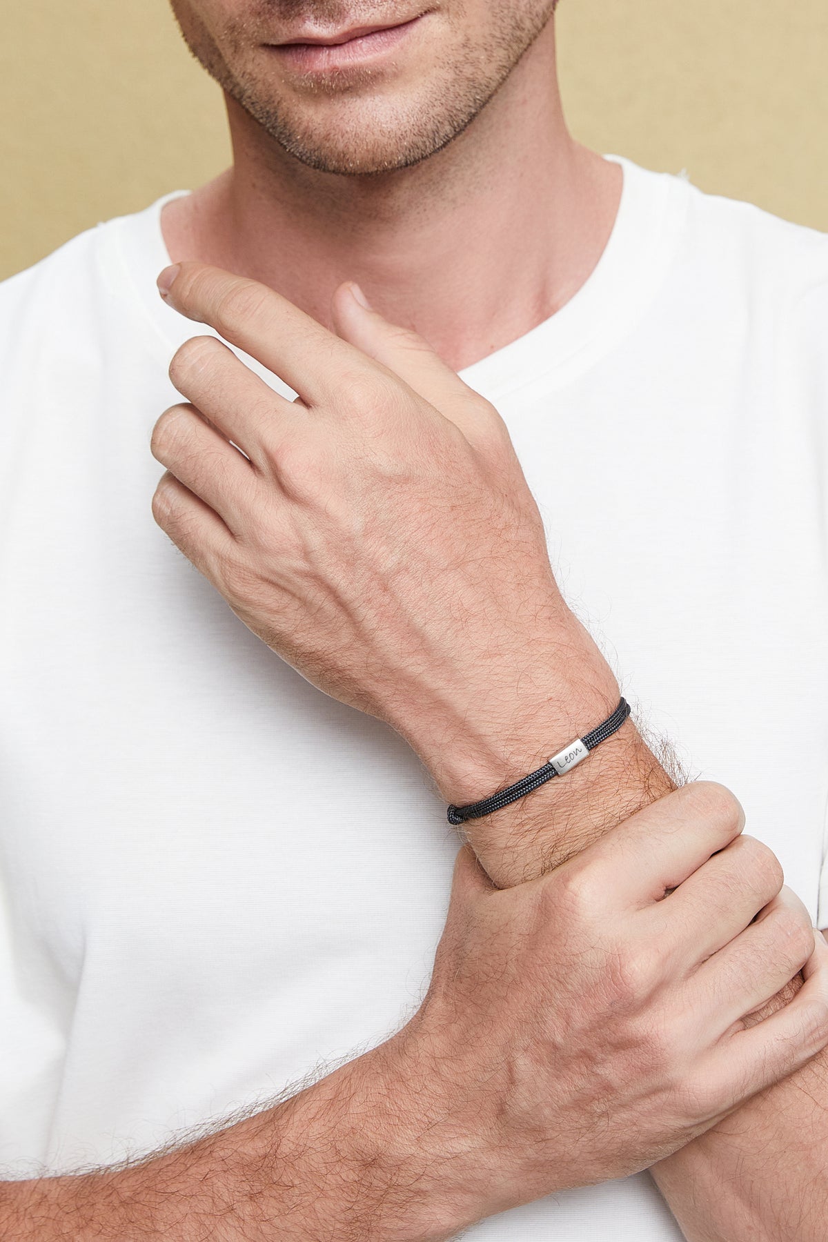 Mann trägt feines Segeltau-Armband in Schwarz mit graviertem Namensschild, verschränkte Arme