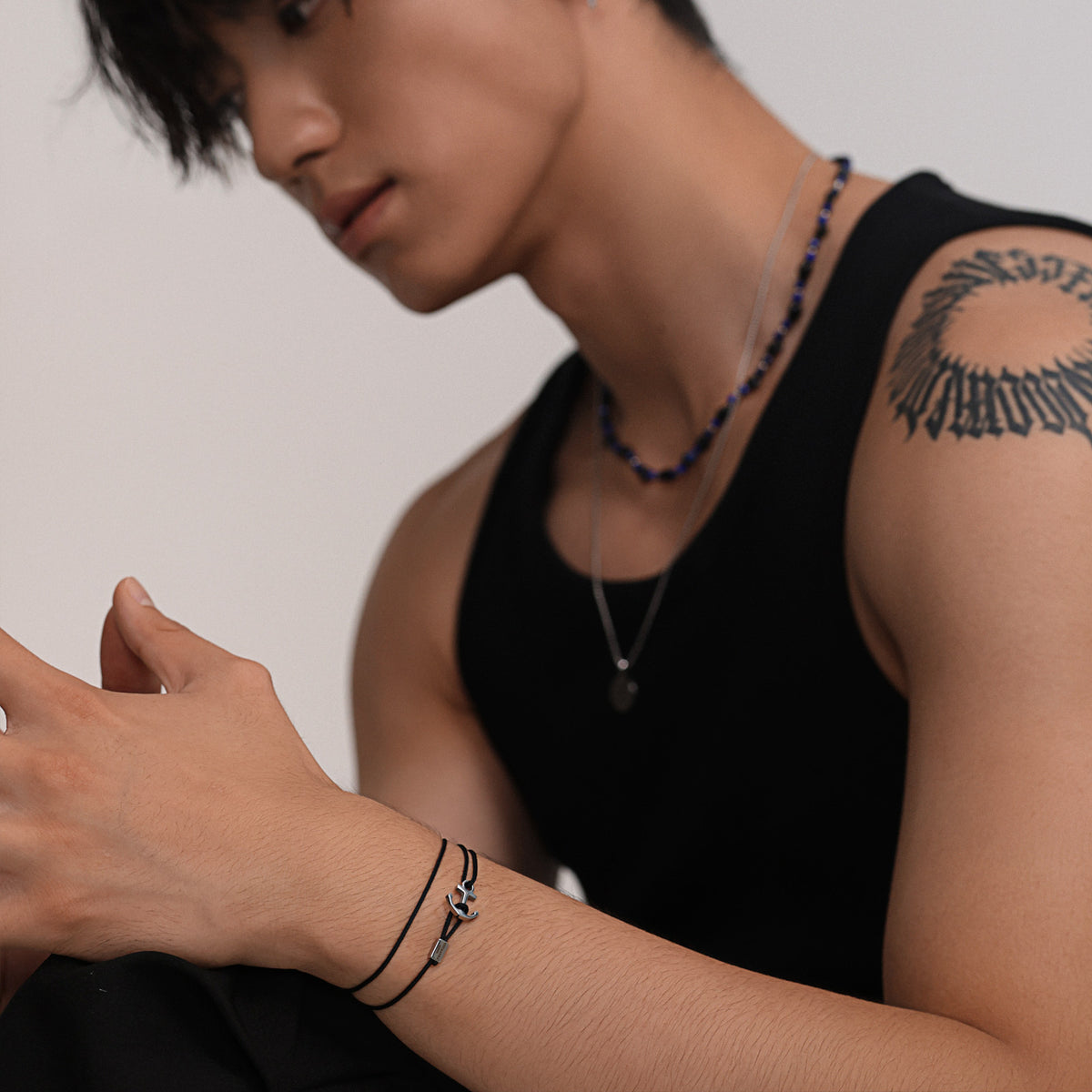 Mann trägt schwarzes Unisex Armband mit Ankerhaken & Gravur am Handgelenk, mit Perlenkette am Hals