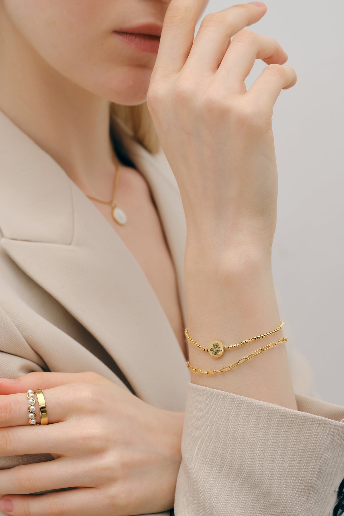 Frau trägt Geburtsblumen-Armband mit rundem Plättchen in Gold, kombiniert mit Ring