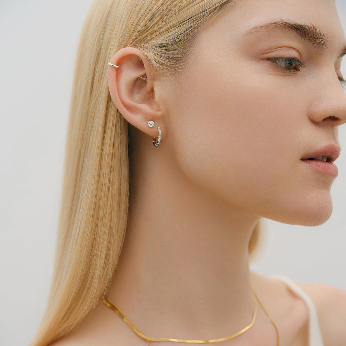 Frau trägt kleine personalisierte runde Ohrstecker in Gold kombiniert mit Creole und Ohrmanschette