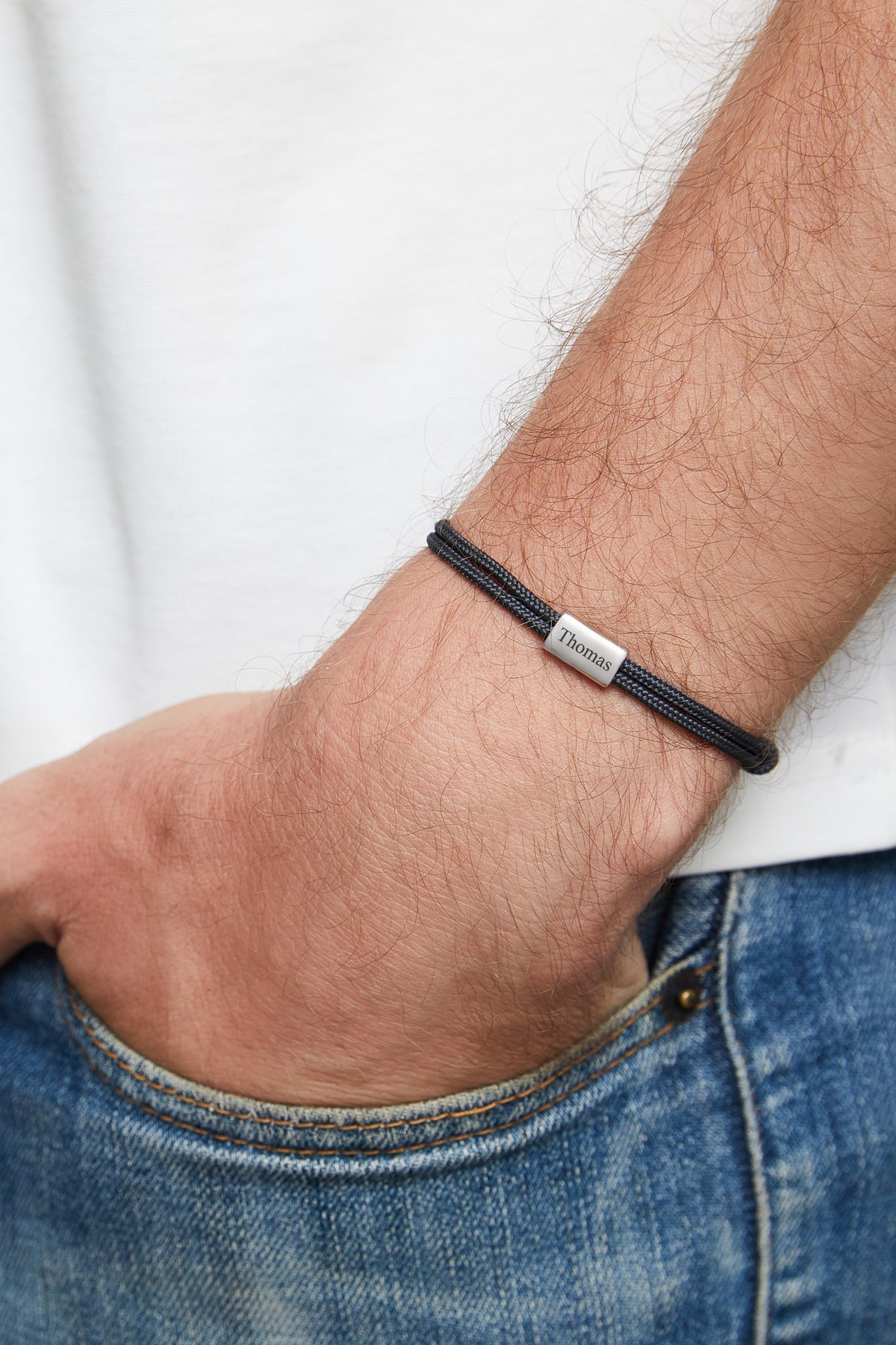 Mann trägt feines Segeltau-Armband in Schwarz mit Gravur 'Thomas', Hand in Jeanstasche