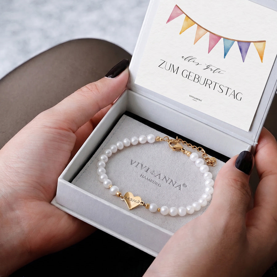 Hände halten Geschenkbox mit Geburtstagskarte und Perlenarmband mit graviertem Goldherz