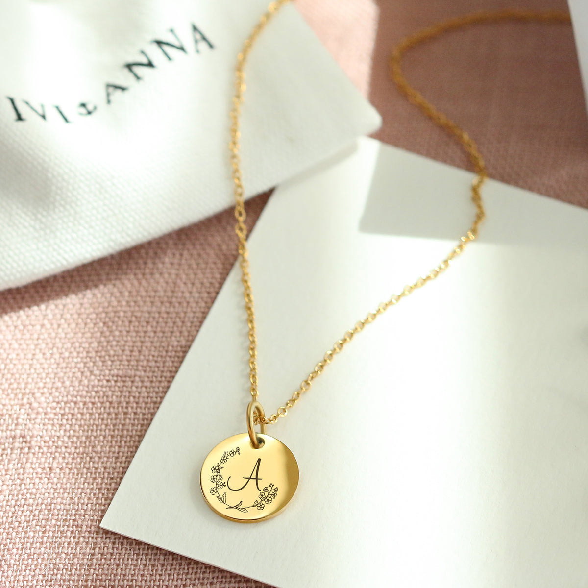 Personalisierte Goldkette mit gravierter Initiale und Blumenkranz-Motiv auf Geschenkkarte
