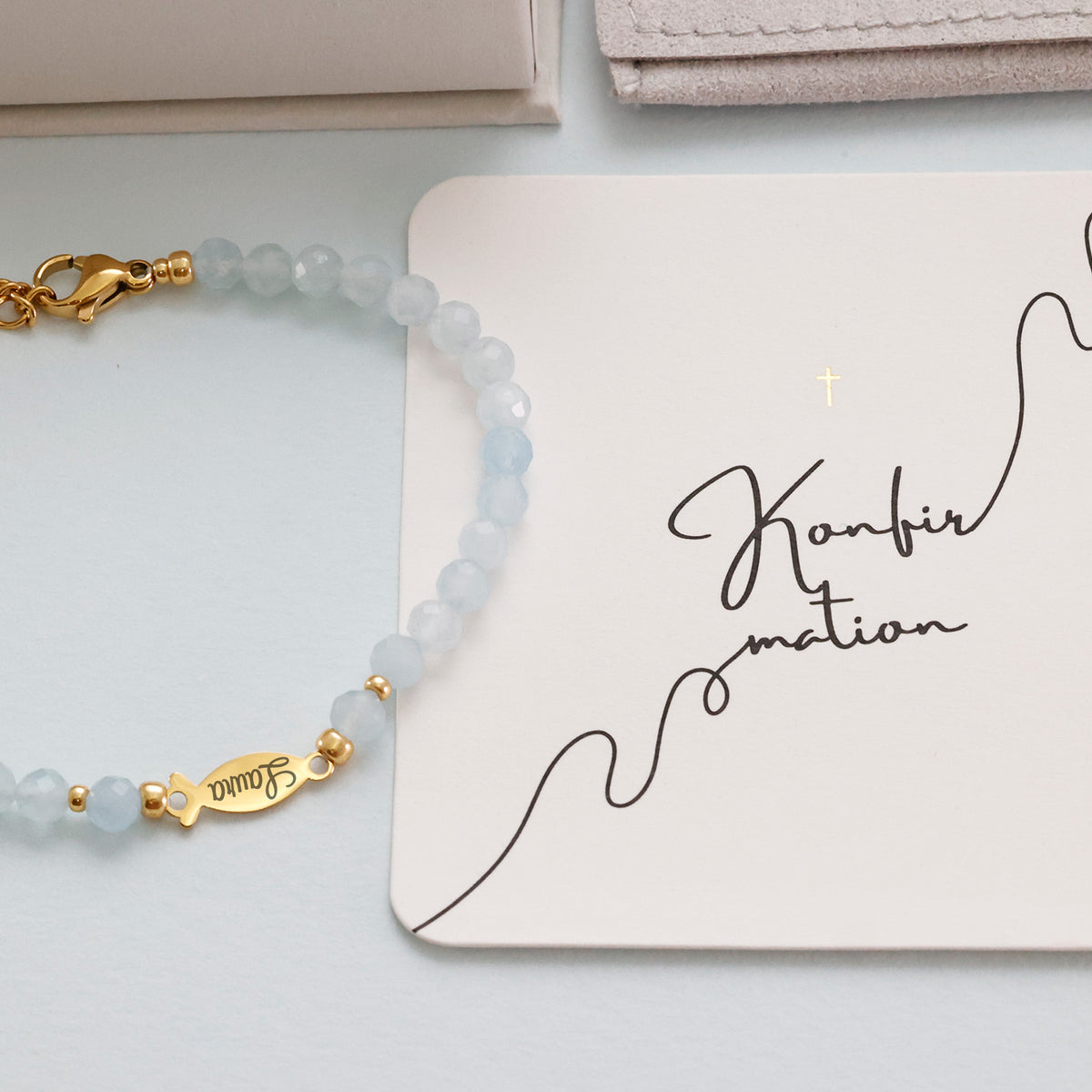 Aquamarin Ichthys-Armband neben handschriftlicher Konfirmations-Grußkarte, Fischanhänger graviert 'Laura'