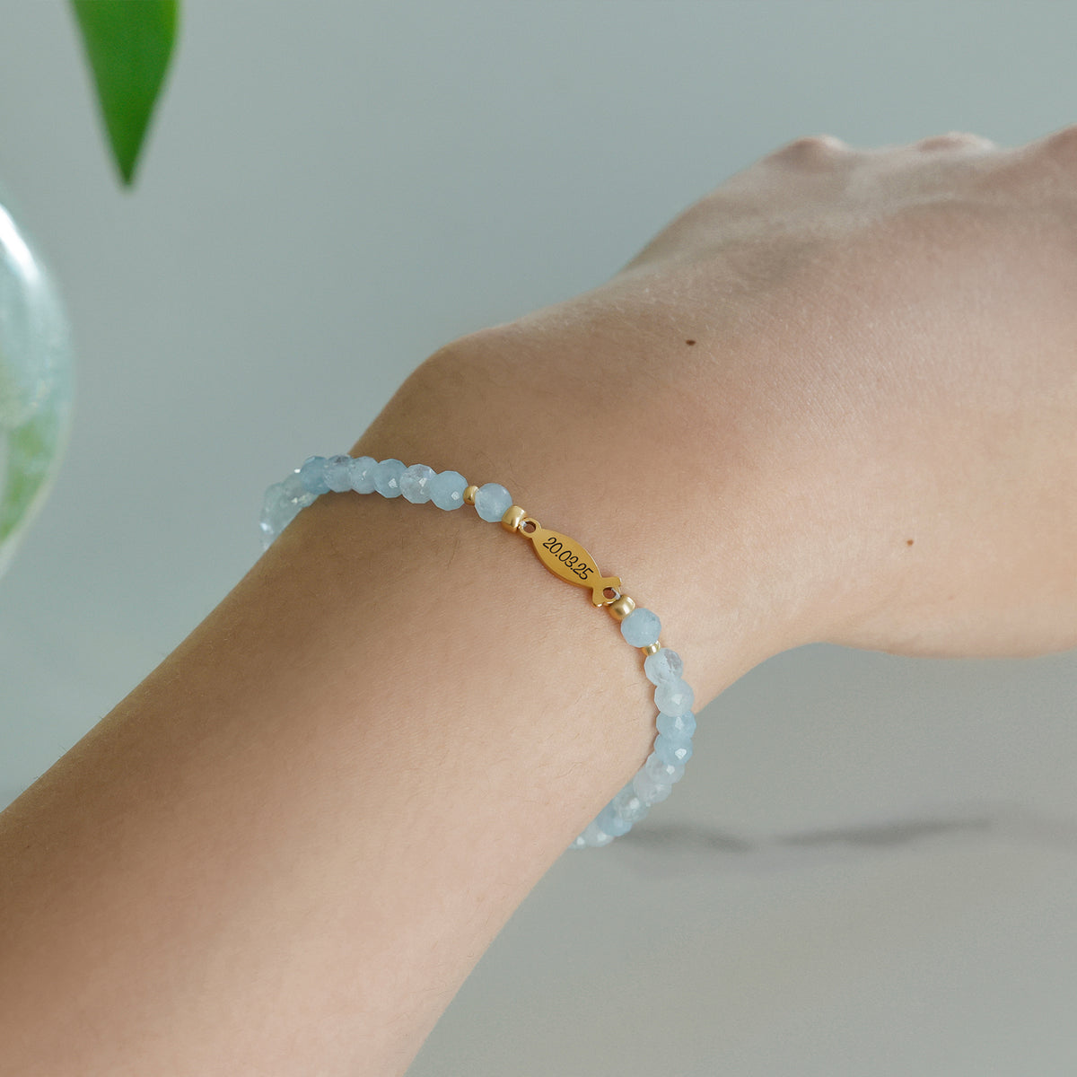 Frau trägt Aquamarin Ichthys-Armband am Handgelenk, Fischanhänger mit graviertem Datum