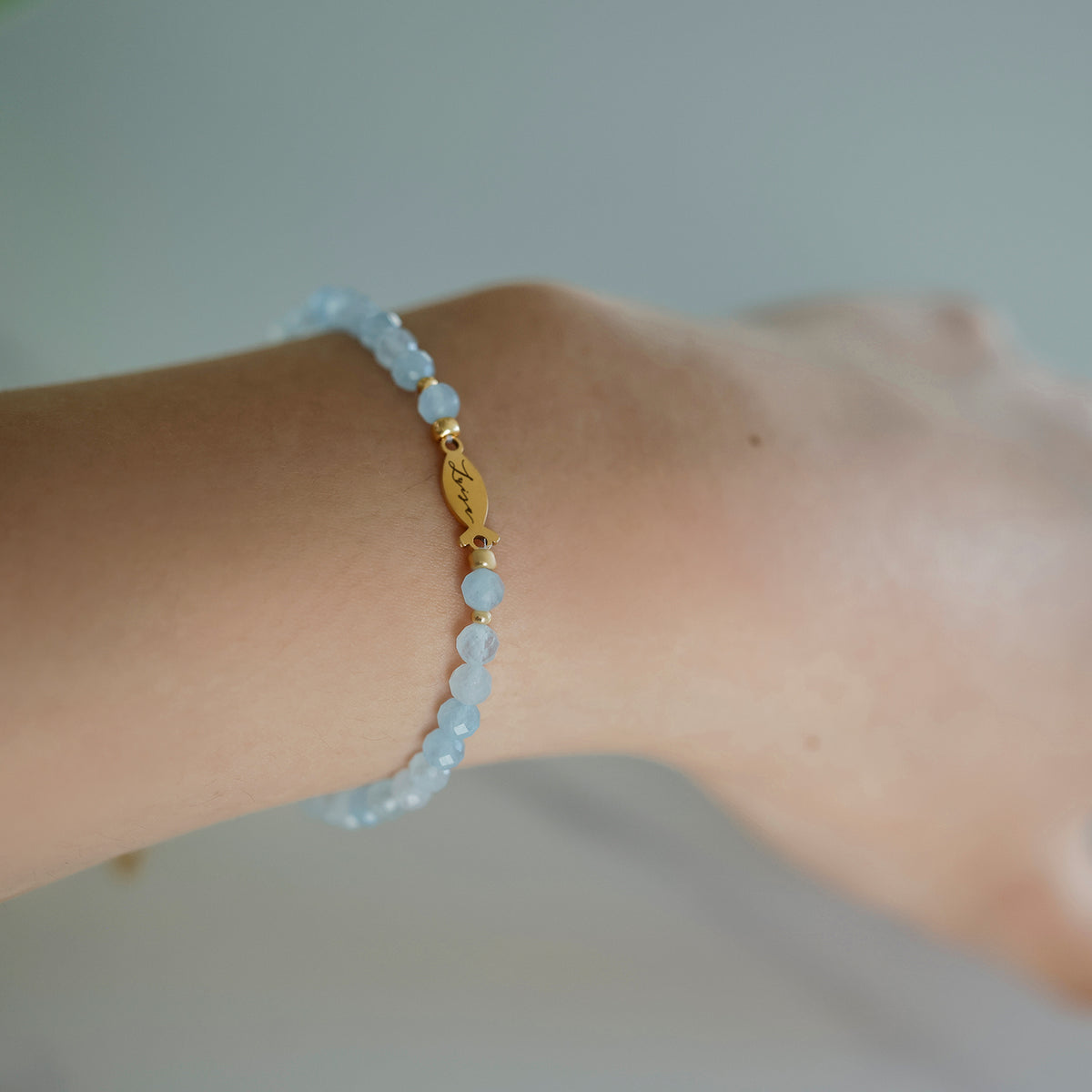 Frau trägt Aquamarin Ichthys-Armband, Nahaufnahme des gravierten Fischanhängers am Arm