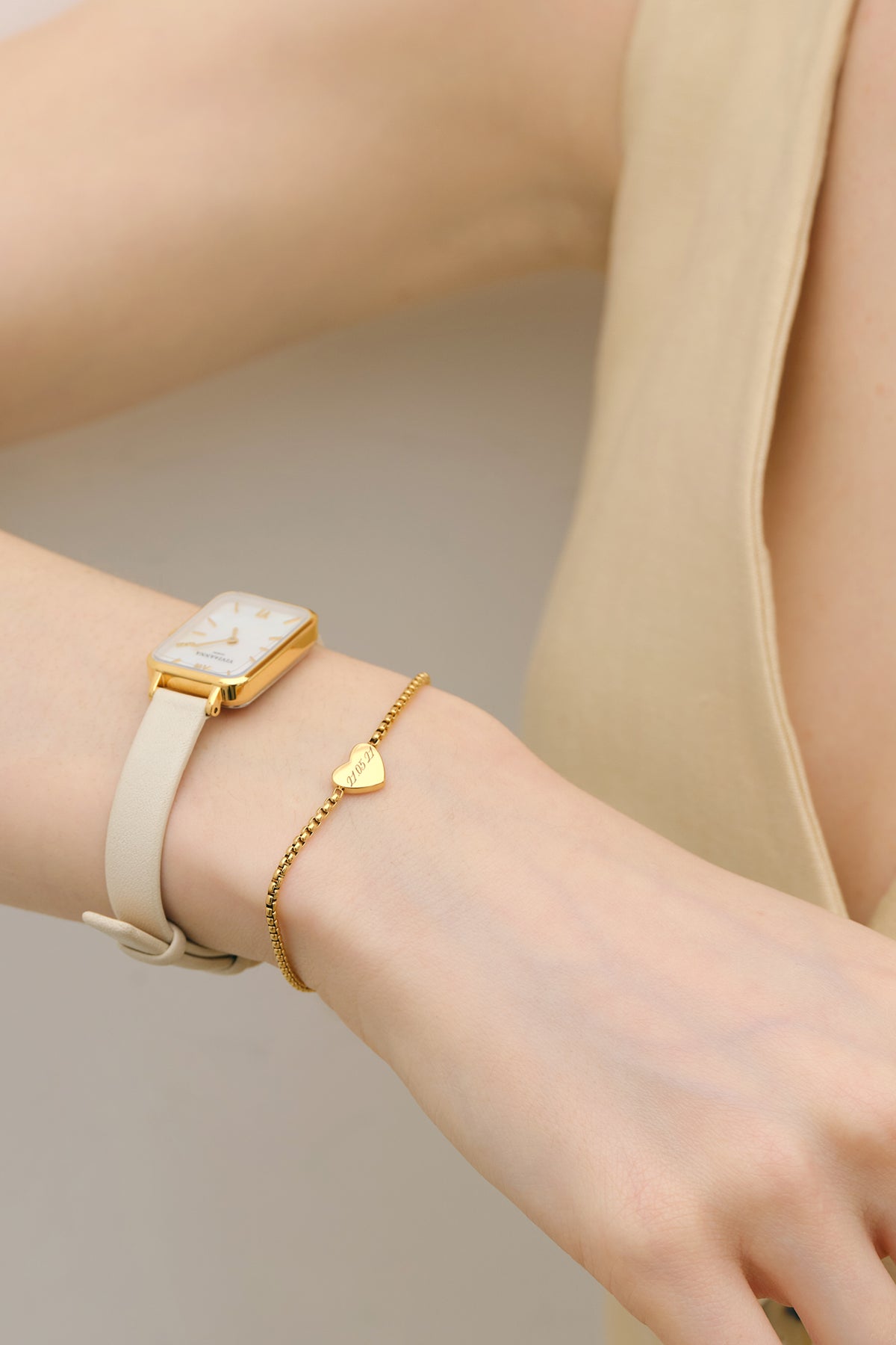 Frau trägt personalisiertes Herz-Armband in Gold am Handgelenk neben einer Armbanduhr