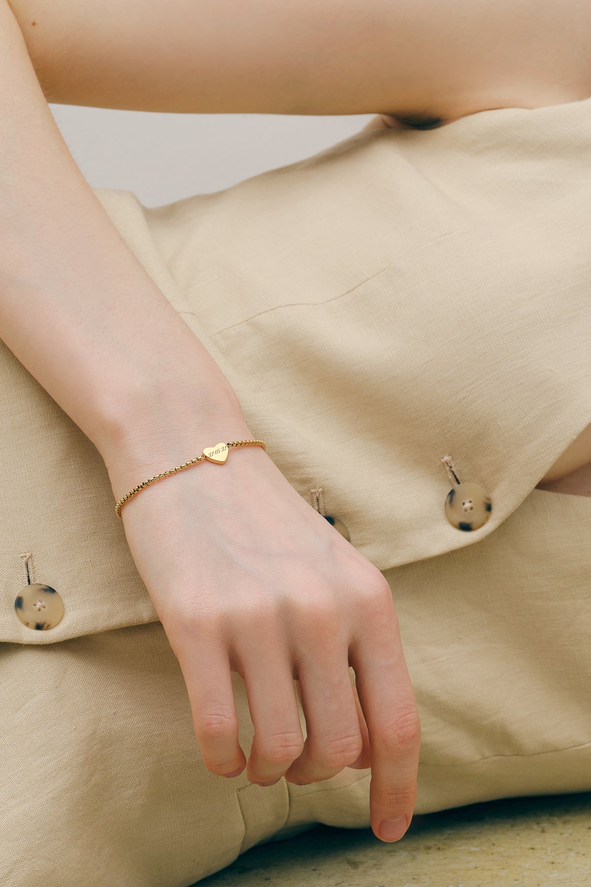 Frau trägt personalisiertes Herz-Armband in Gold am Handgelenk in lässiger Sitzpose