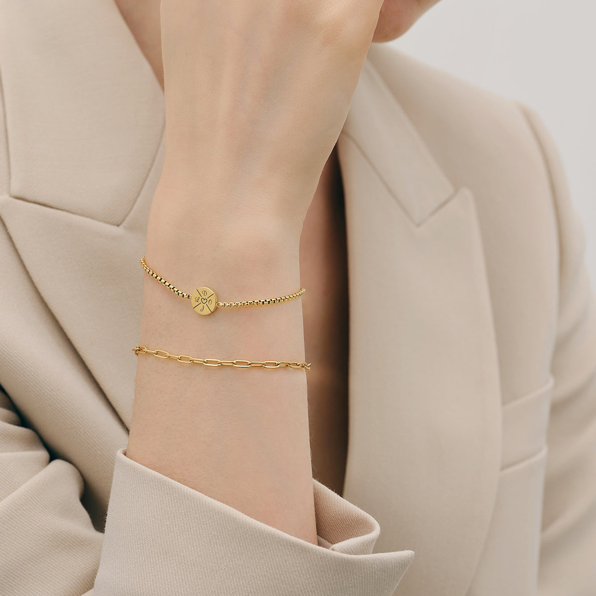 Frau trägt goldenes Armband mit Gravur, kombiniert mit Gliederkette am Handgelenk