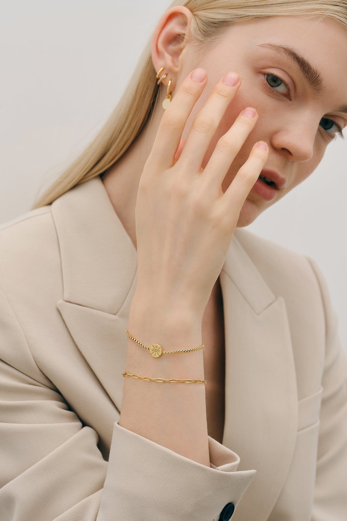 Frau trägt goldenes Armband mit Gravur am Handgelenk, Nahaufnahme mit Ohrringen im Hintergrund