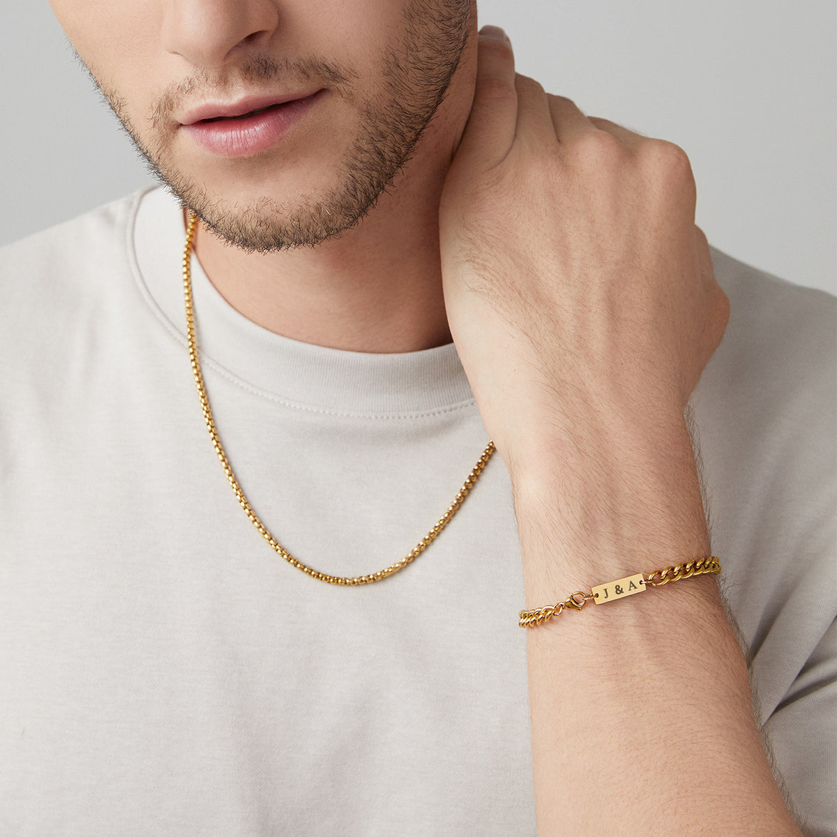 Mann trägt goldenes Panzerarmband mit Gravurplättchen 'J & A' und Ankermotiv am Handgelenk