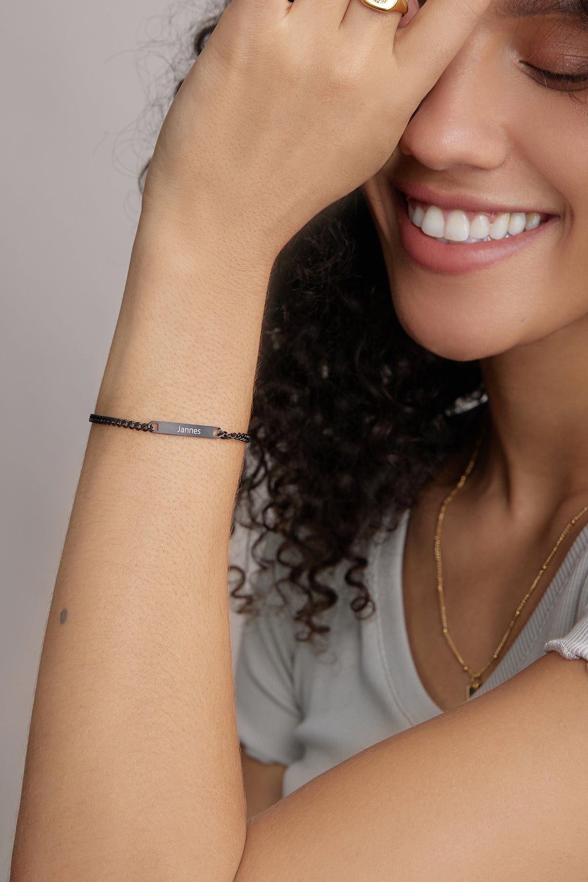 Lächelnde Frau trägt schwarzes personalisiertes Armband mit dem Namen 'Jannes' am Handgelenk