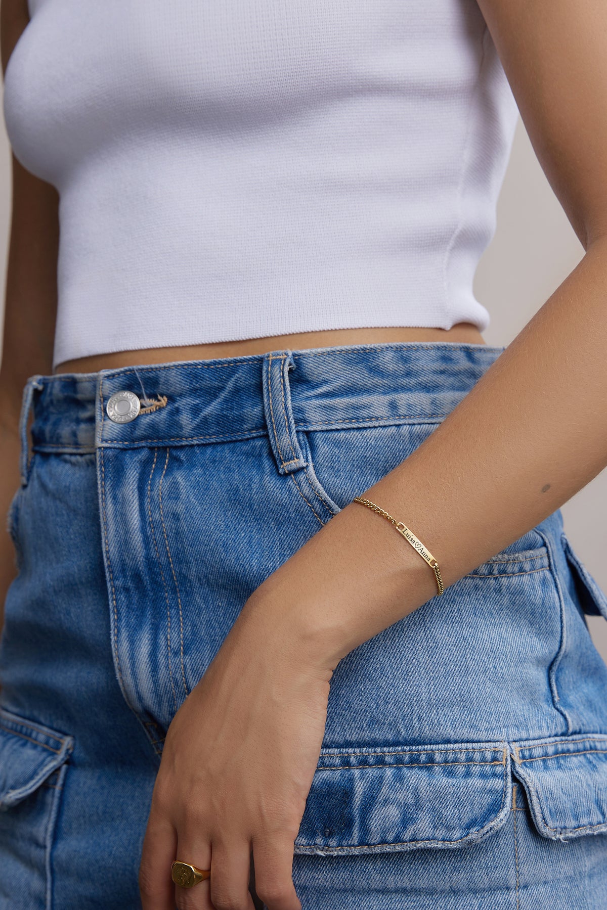 Frau trägt goldenes personalisiertes Armband am Handgelenk vor Jeans, Nahaufnahme