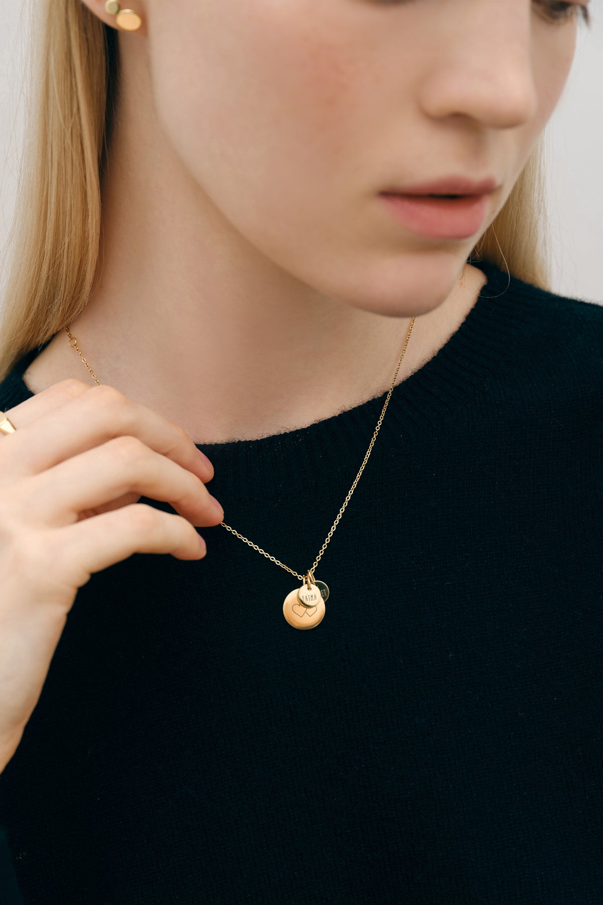 Frau hält goldene Familienkette mit rundem Plättchen mit Herzmotiv in der Hand