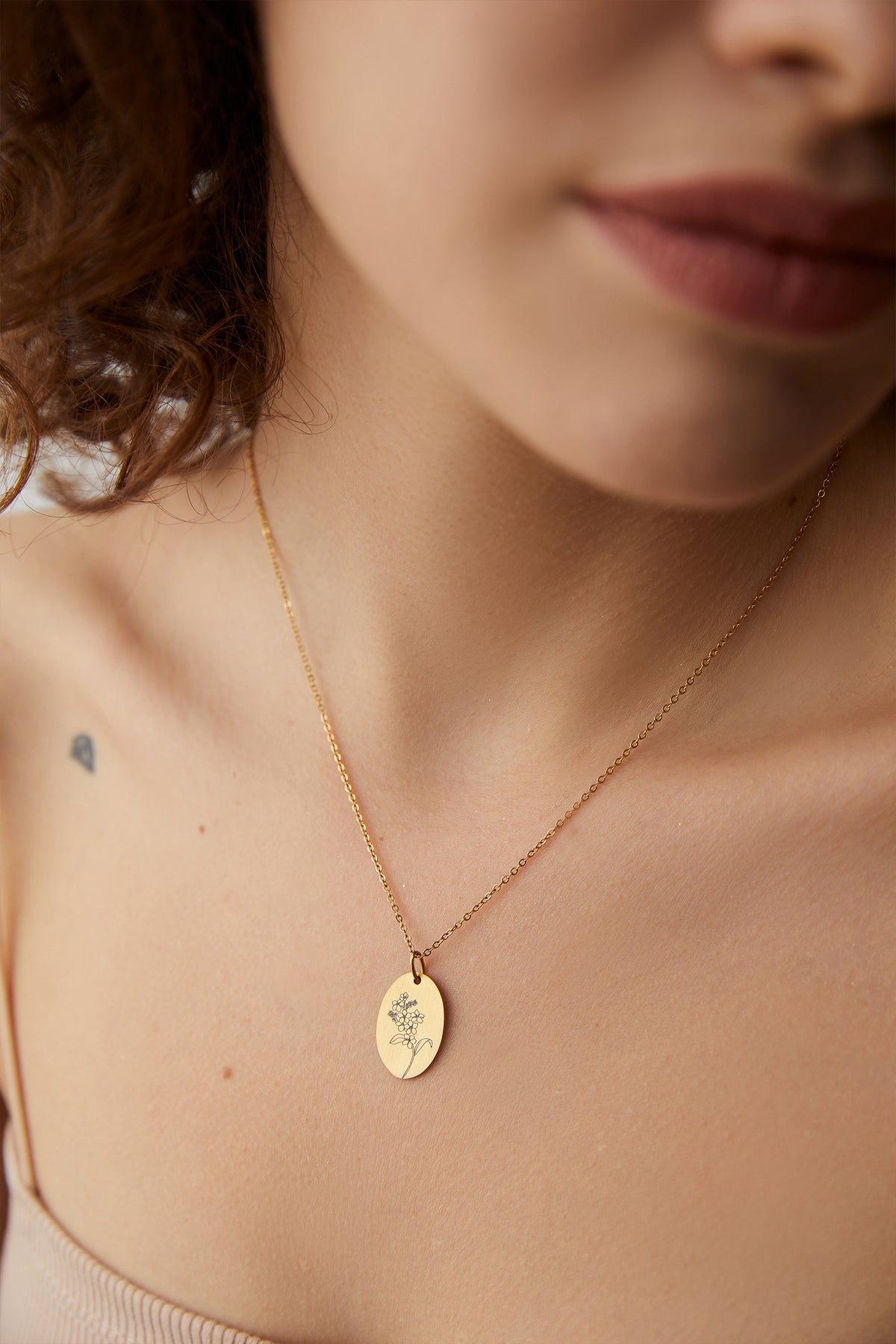 Frau trägt Kette mit graviertem Ovalanhänger in Gold mit Blumenmotiv, Nahaufnahme