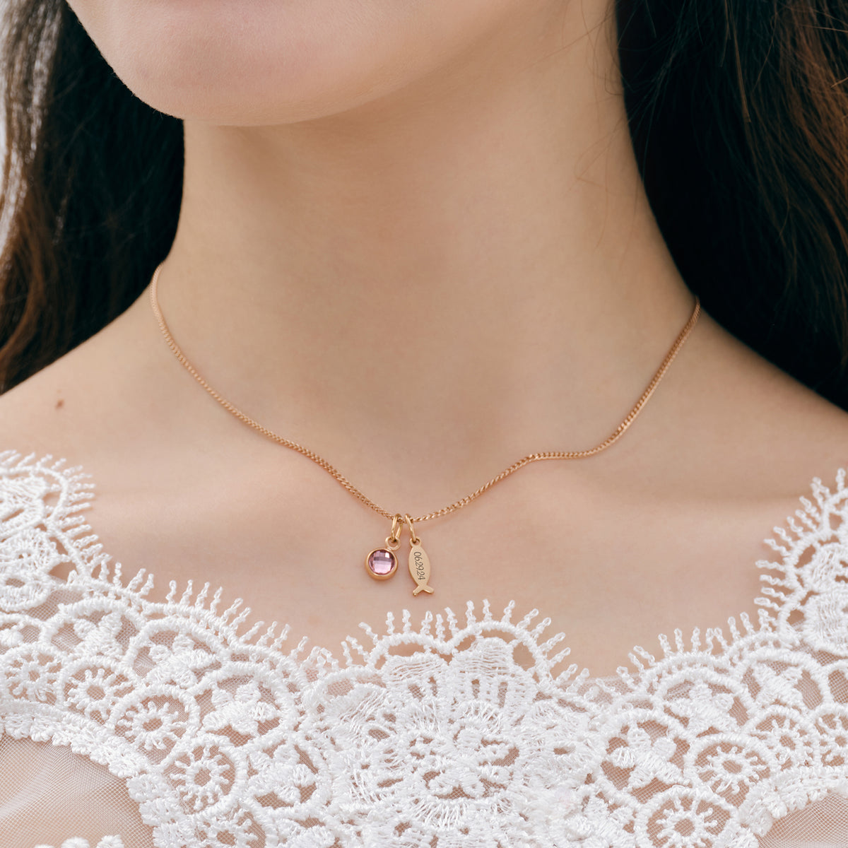 Ichthys Kette mit Geburtsstein – Nahaufnahme Mädchen trägt goldene Kette mit Fisch-Anhänger und rosa Stein
