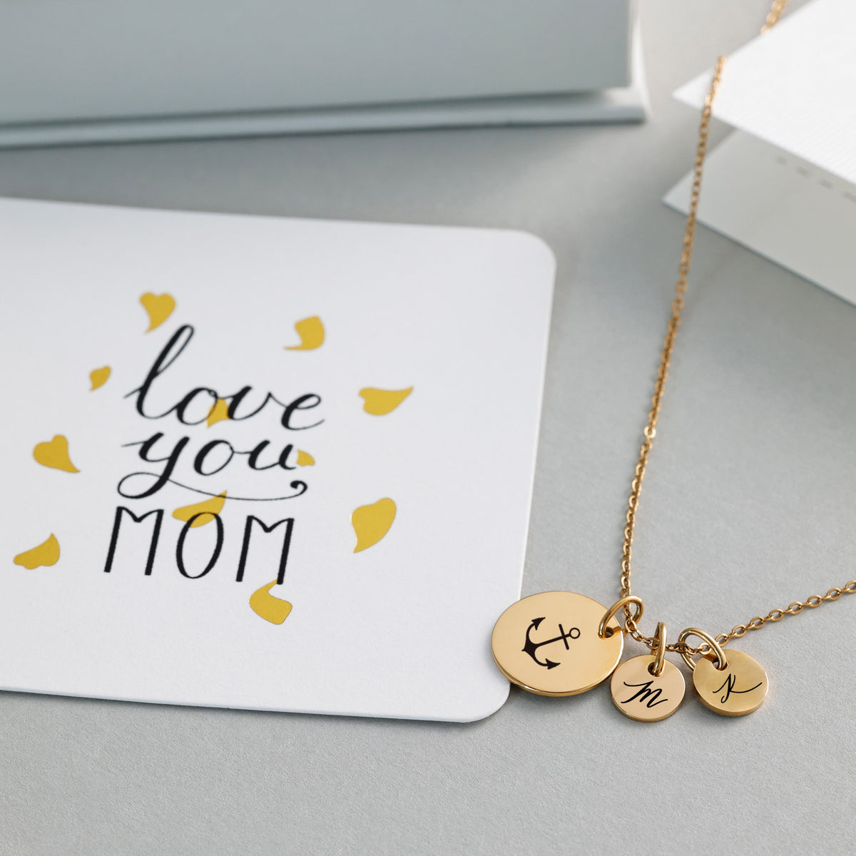Plättchen-Kette mit Wunschgravur in Gold mit Anker-Symbol und Initialen, auf Grußkarte 'Love you Mom'