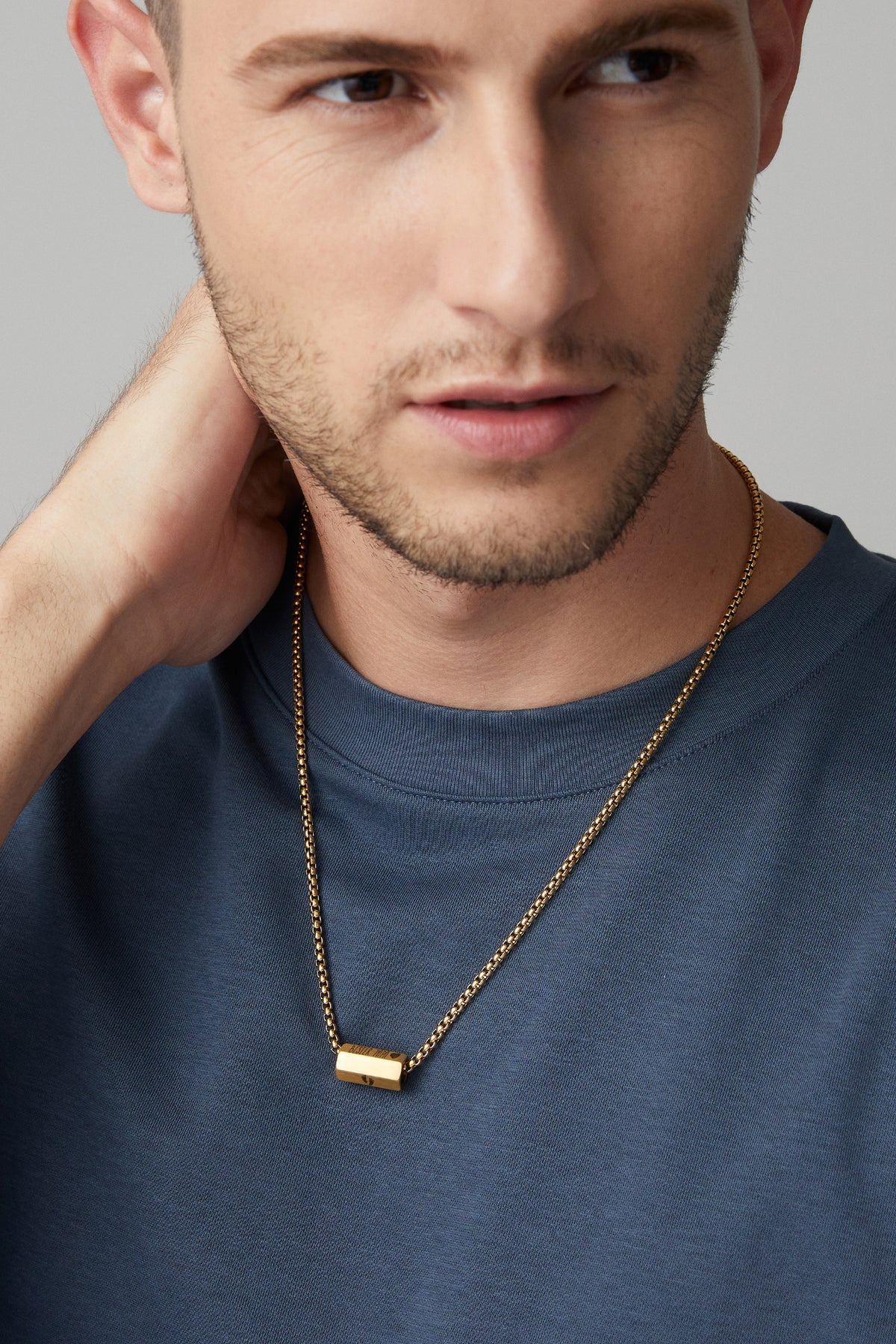 Mann trägt goldene Kette mit rechteckigem Gravur-Anhänger über blauem Pullover