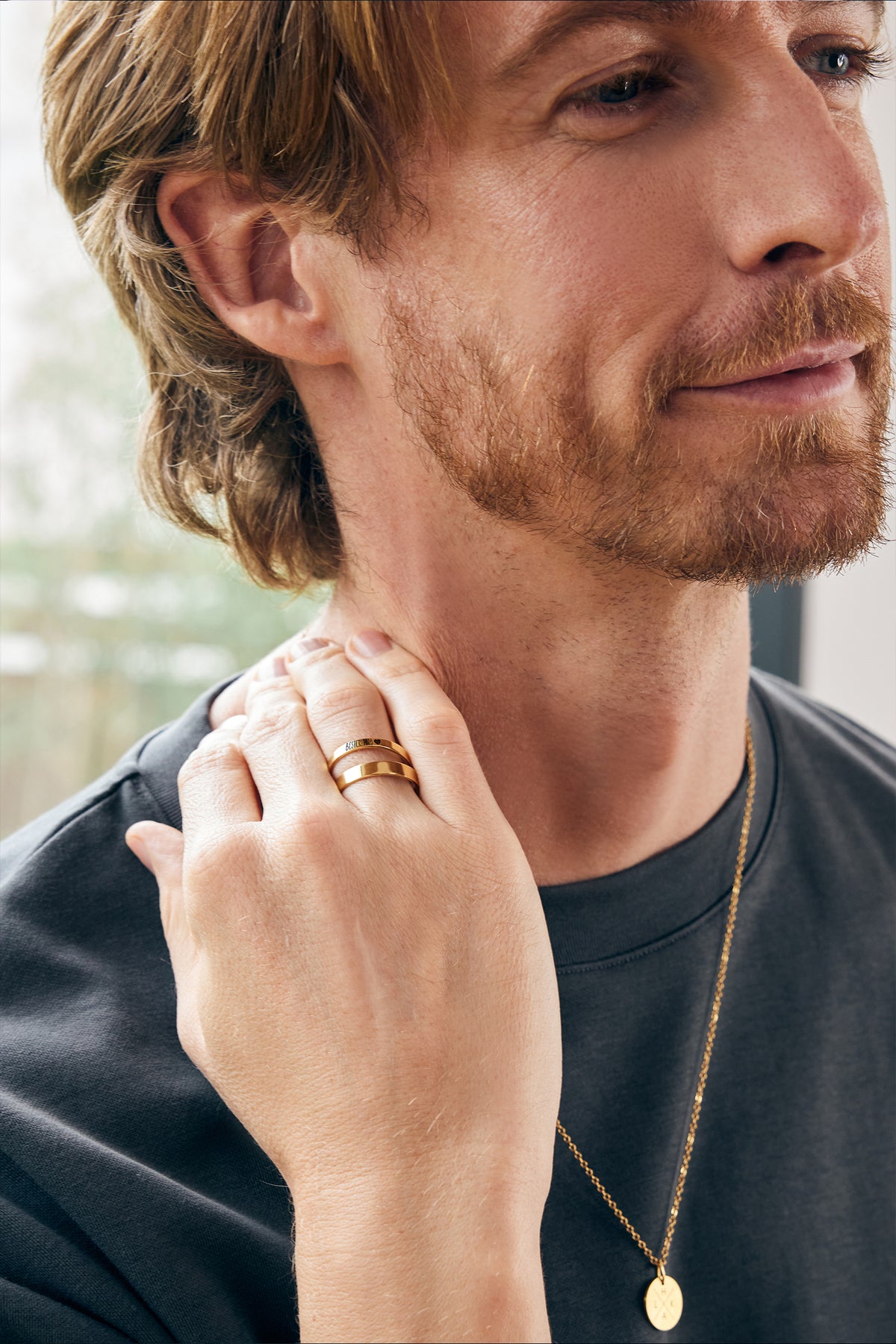Mann trägt goldenen Gravur-Ring und goldene Kette mit rundem Anhänger am Hals