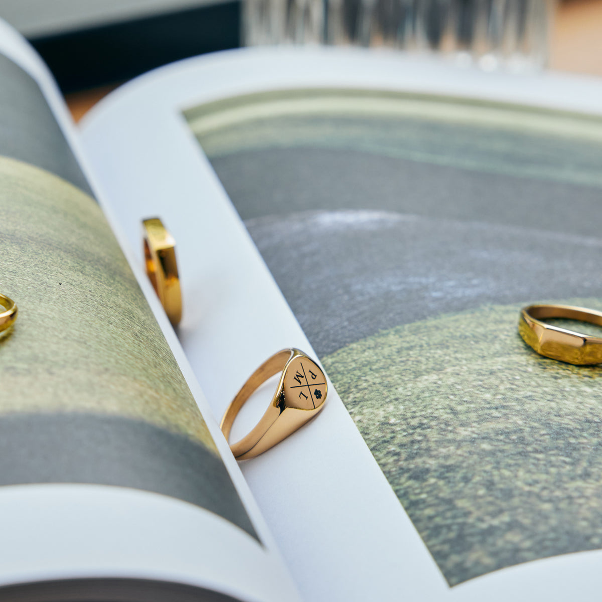 Runder Siegelring mit Gravur in Gold – mehrere Ringe mit Quadranten-Design auf einem Buch