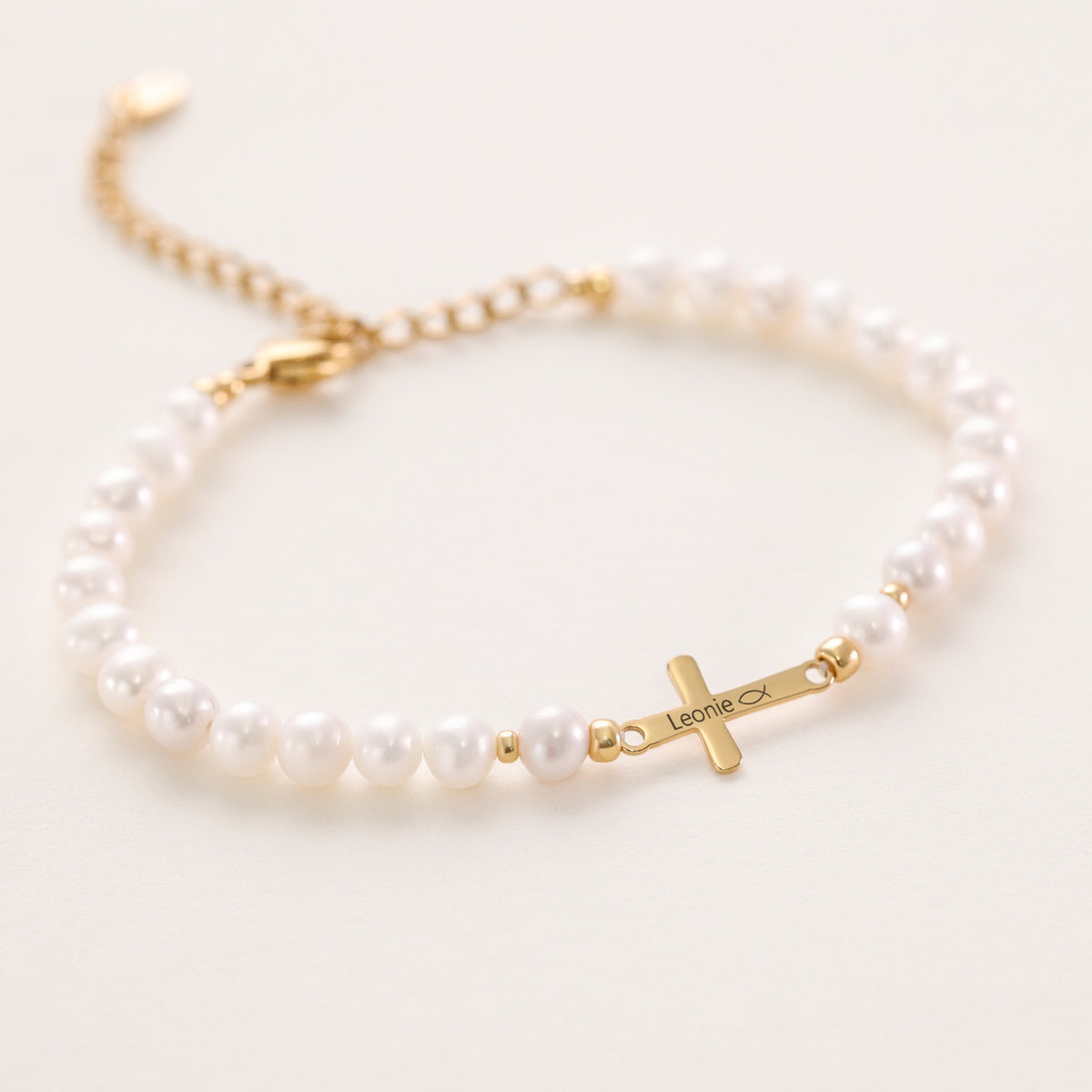 Süßwasserperlen Kreuz-Armband mit goldenem Kreuz, Gravur 'Leonie' und Ichthys-Symbol in Nahaufnahme