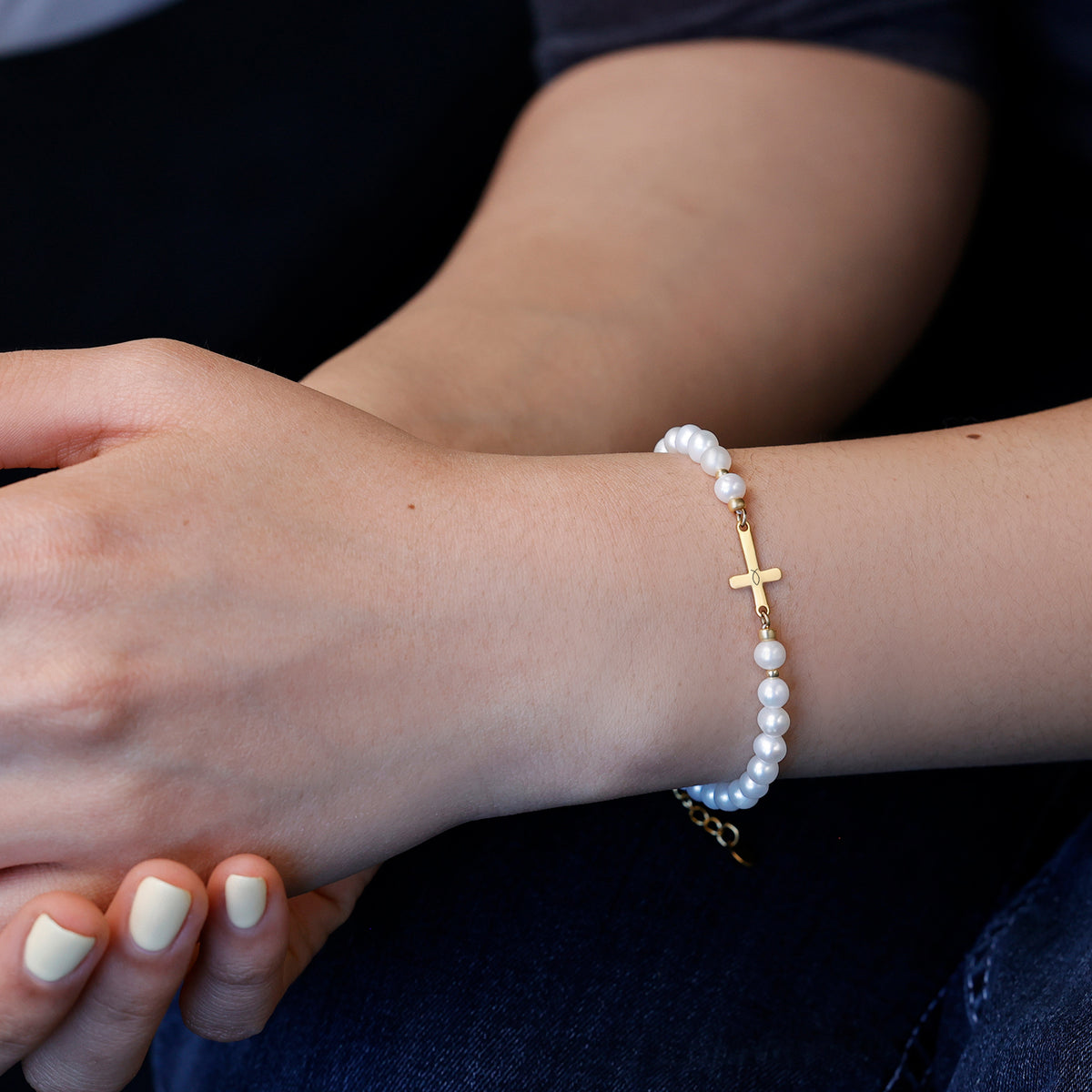 Frau trägt Süßwasserperlen Kreuz-Armband am Arm, kombiniert mit goldener Figaro-Kette