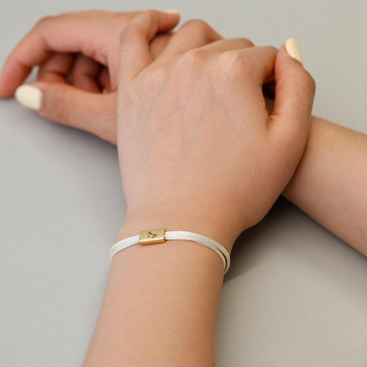 Kind trägt weißes Kinder Satinband Armband mit Gravur, Hände ineinander verschränkt