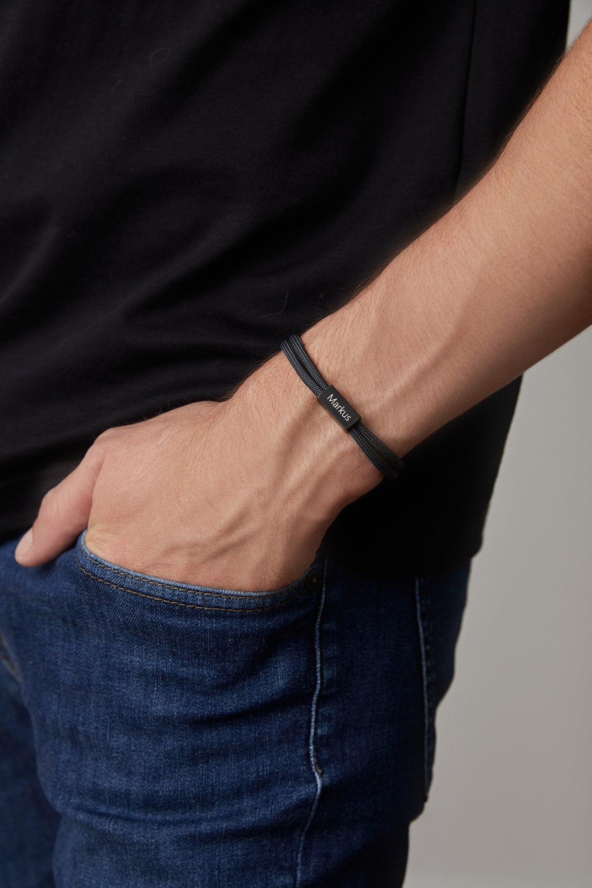 Mann trägt schwarzes Segeltau-Armband mit Gravur Markus, Hand in Hosentasche