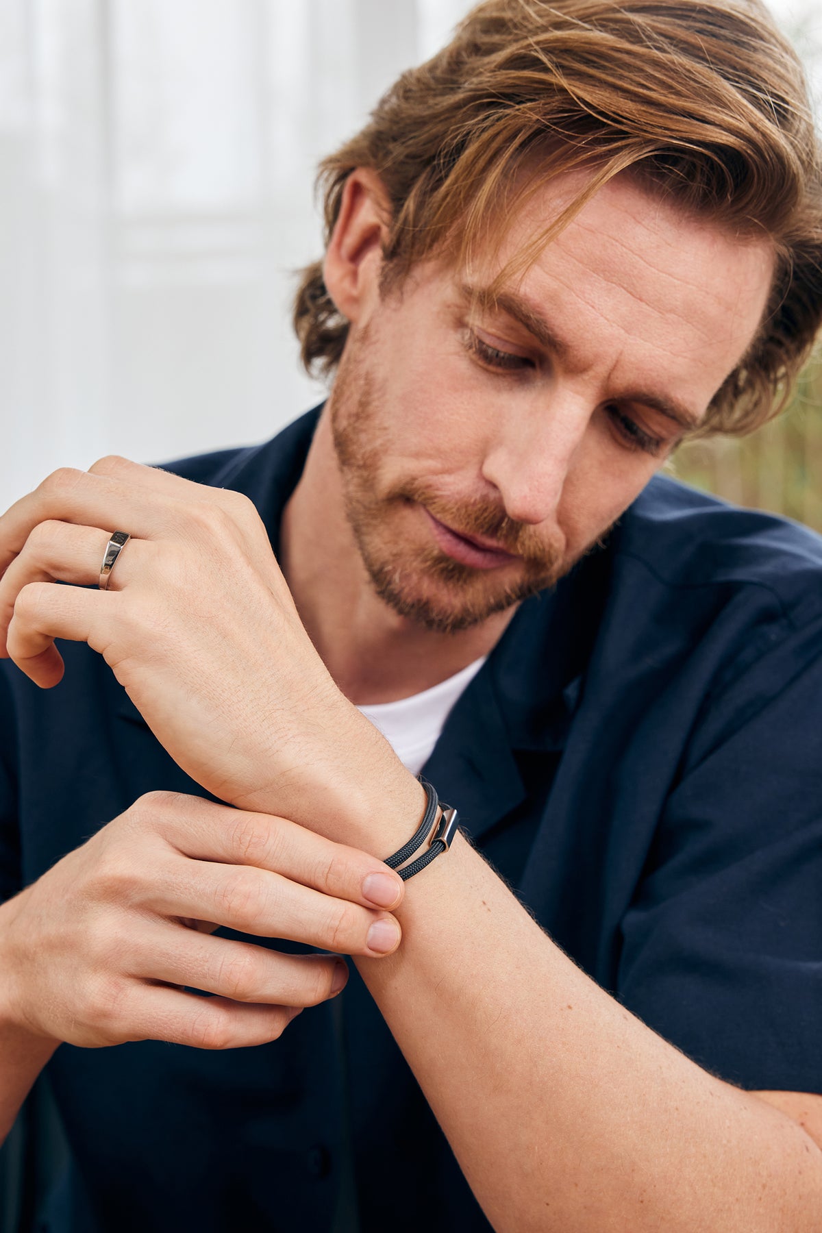 Mann betrachtet sein schwarzes Segeltau-Armband mit roségoldenem Gravurverschluss am Arm